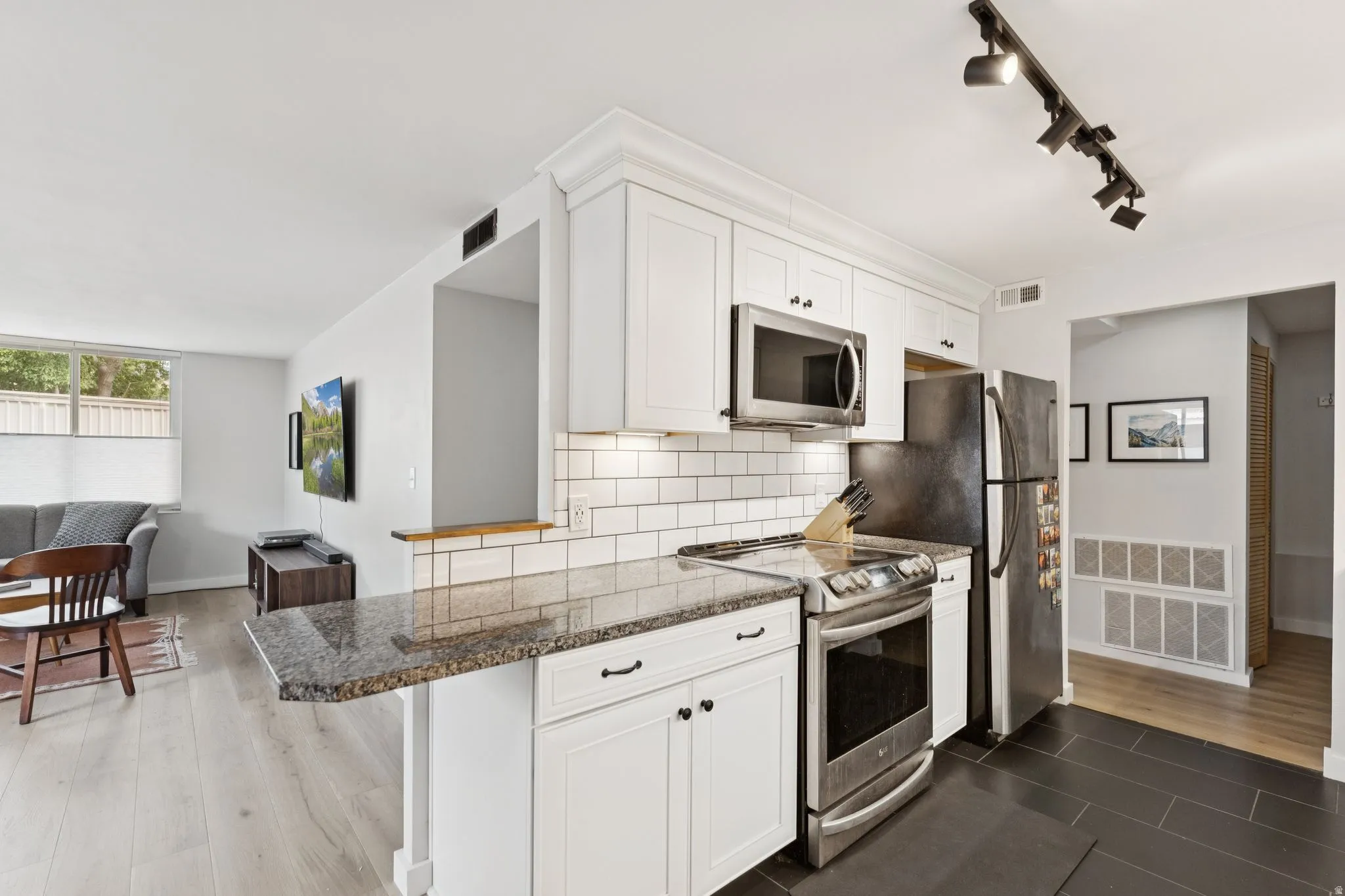 Kitchen featuring stainless steel appliances, track lighting, tasteful backsplash, white cabinets, and dark stone countertops