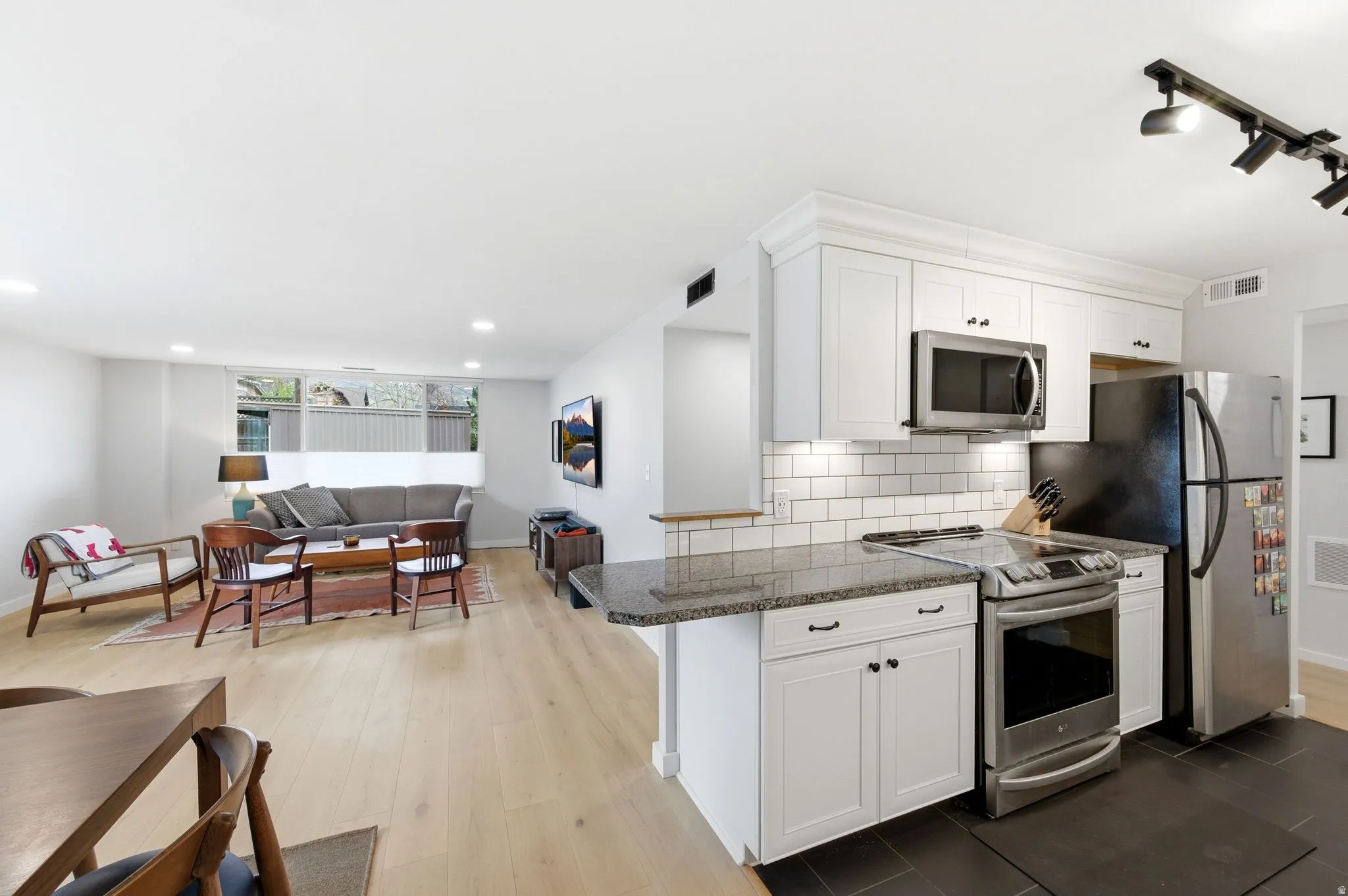 Kitchen featuring stainless steel appliances, dark stone countertops, white cabinetry, open floor plan, and track lighting