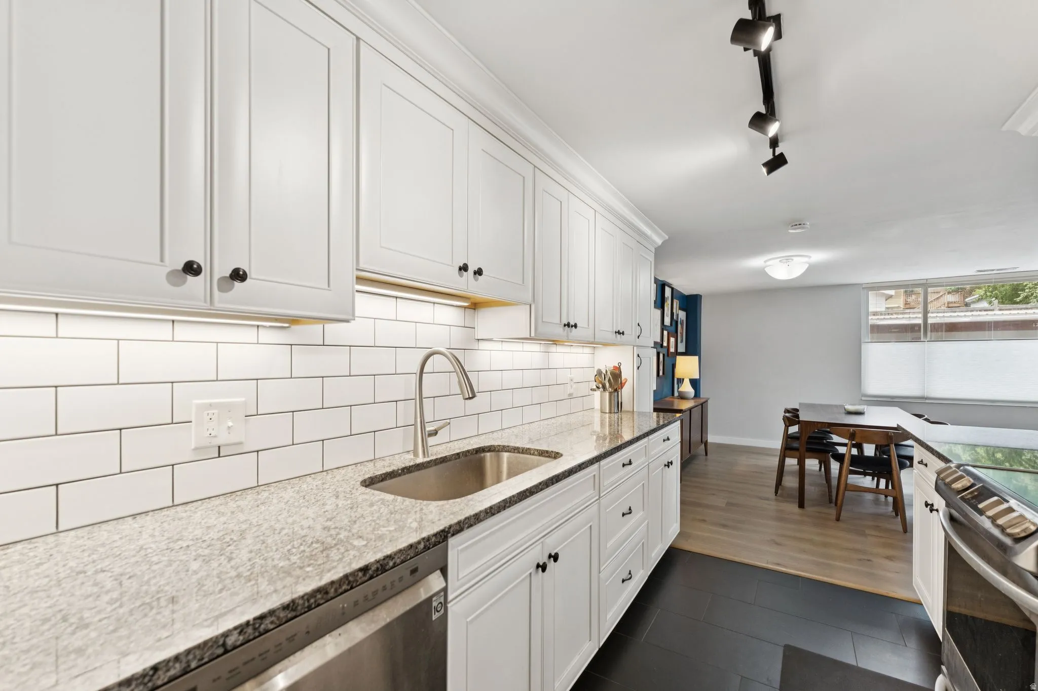 Kitchen featuring track lighting, stainless steel appliances, light stone countertops, white cabinetry, and decorative backsplash