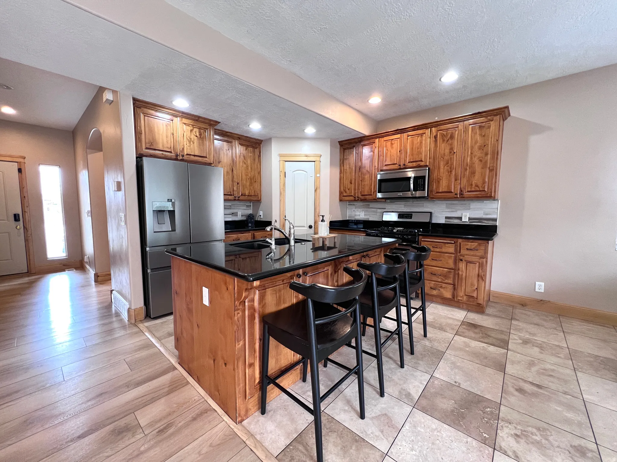 Kitchen with wood finish cabinetry, arched walkways, stainless steel appliances, a kitchen island with sink, and a kitchen bar