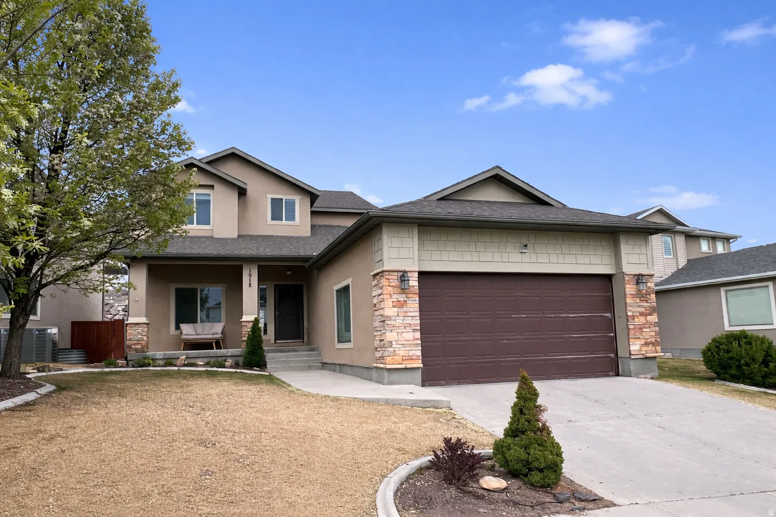 View of front of house featuring a porch, a garage, concrete driveway, stone siding, and stucco siding
