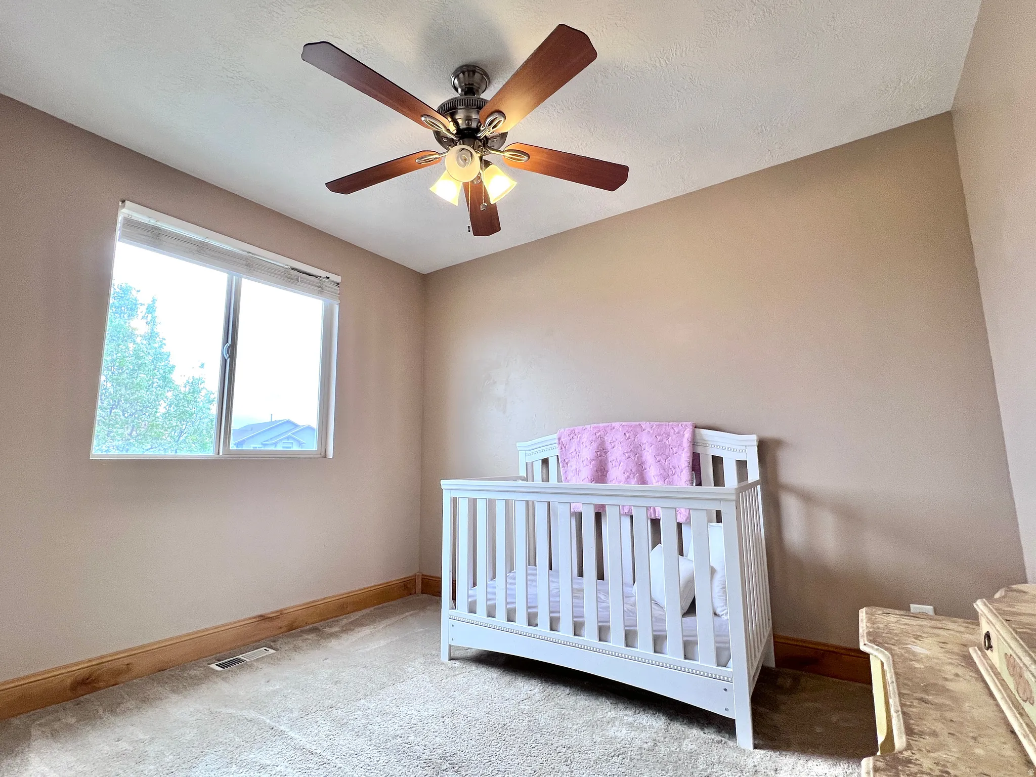 Carpeted bedroom with a crib and ceiling fan