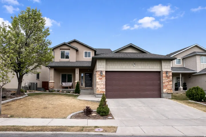 View of front of house featuring a porch, a garage, concrete driveway, stone siding, and stucco siding