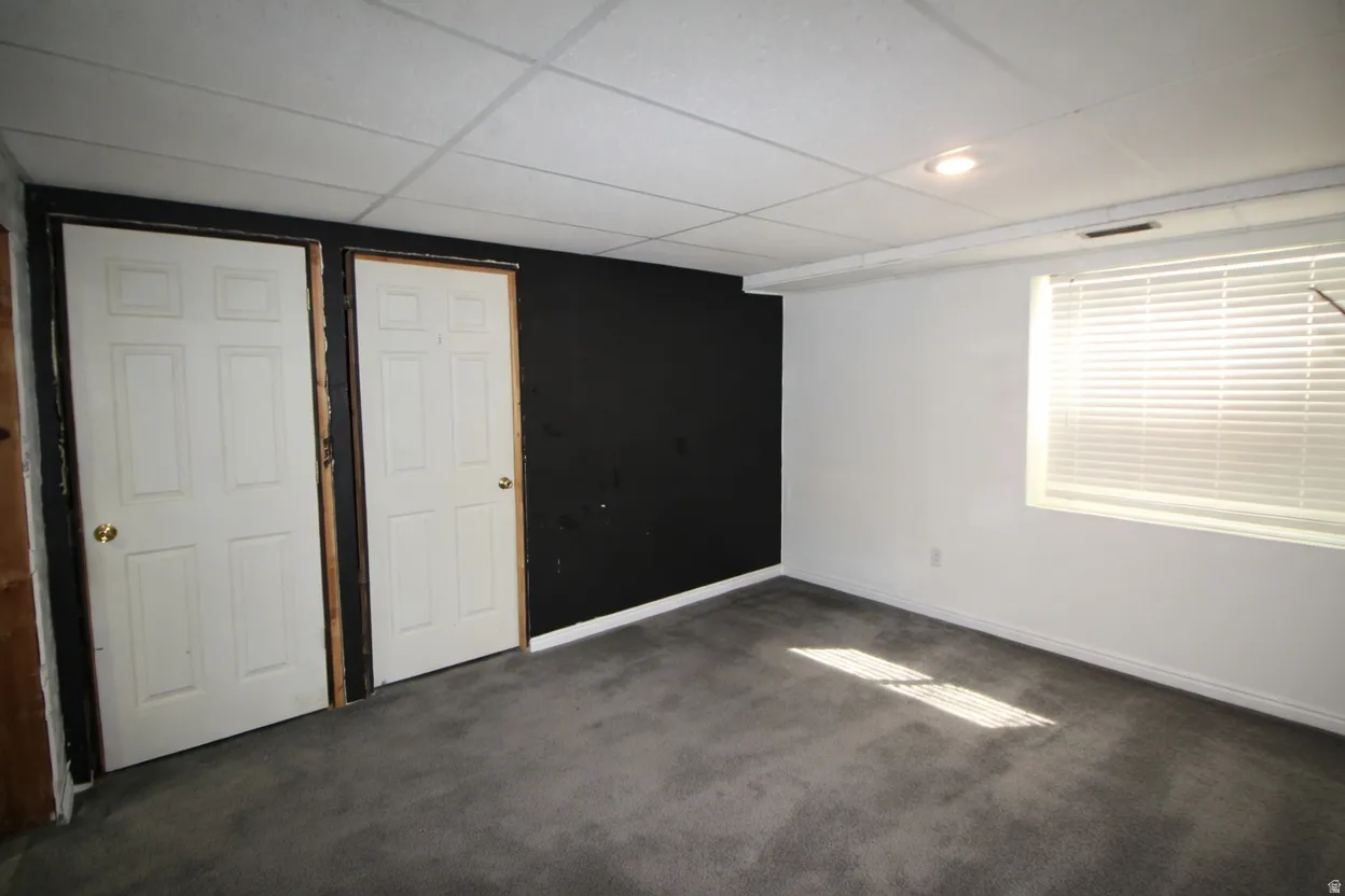 Unfurnished bedroom featuring dark carpet and a drop ceiling