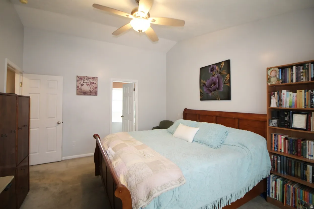 Bedroom with carpet flooring, vaulted ceiling, ensuite bathroom, and a ceiling fan