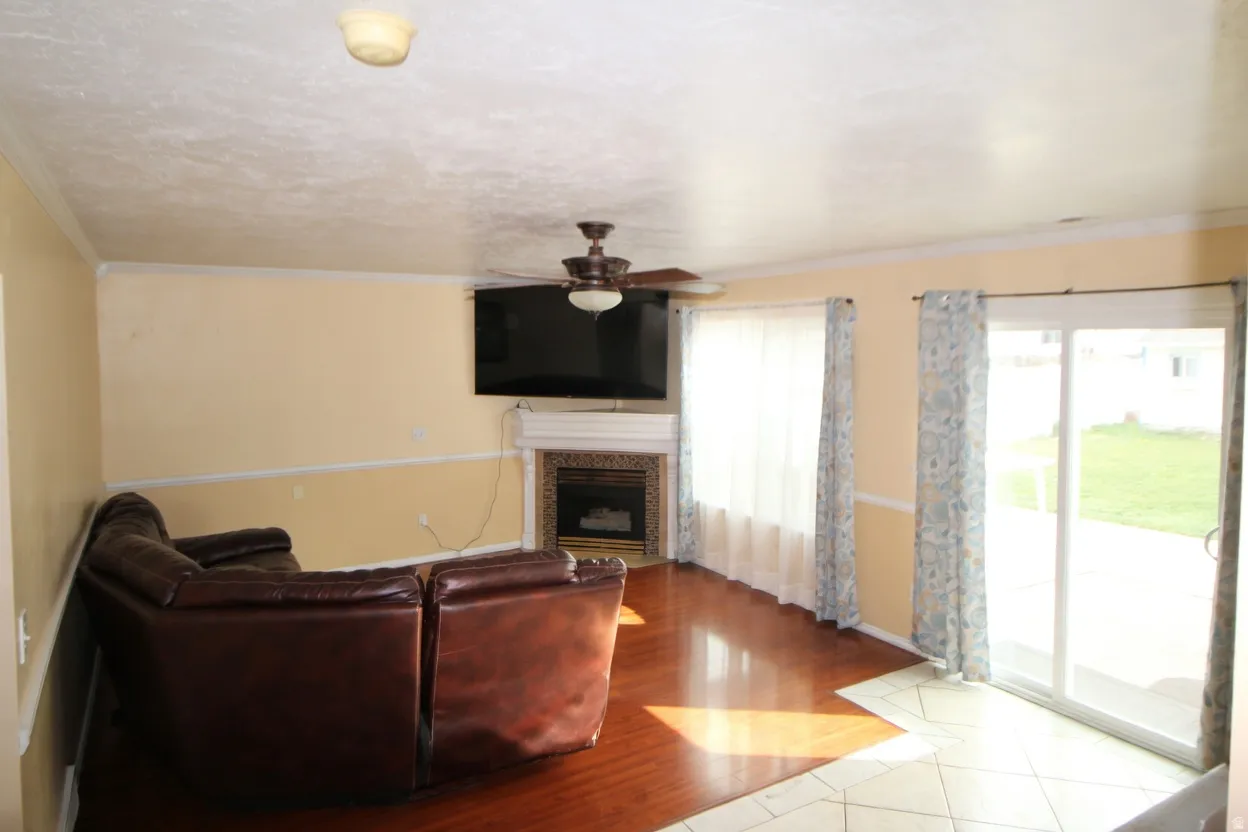 Living room featuring crown molding, ceiling fan, a fireplace, and light wood finished floors