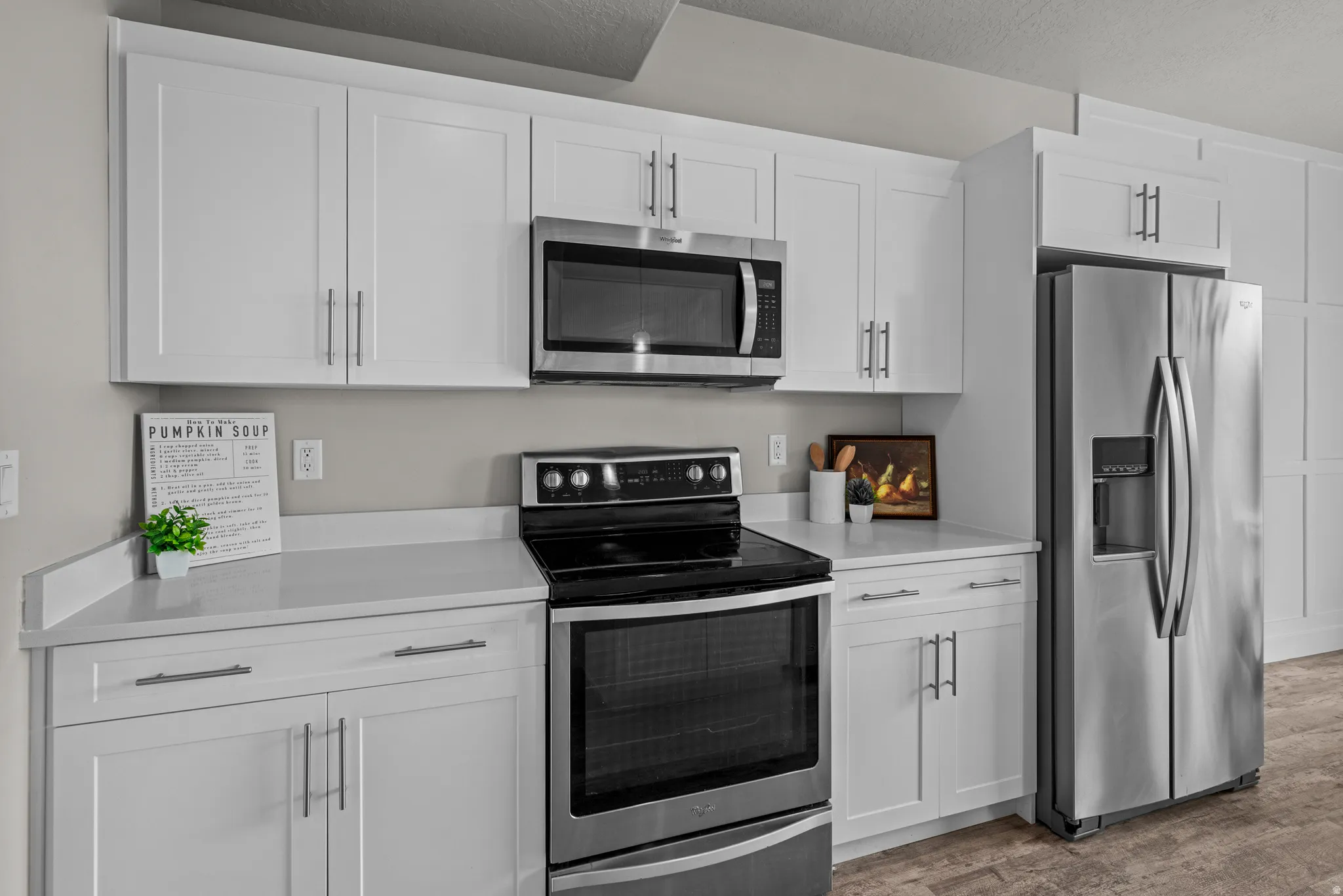 Kitchen with stainless steel appliances, white cabinetry, light wood-style floors, light stone countertops, and a textured ceiling