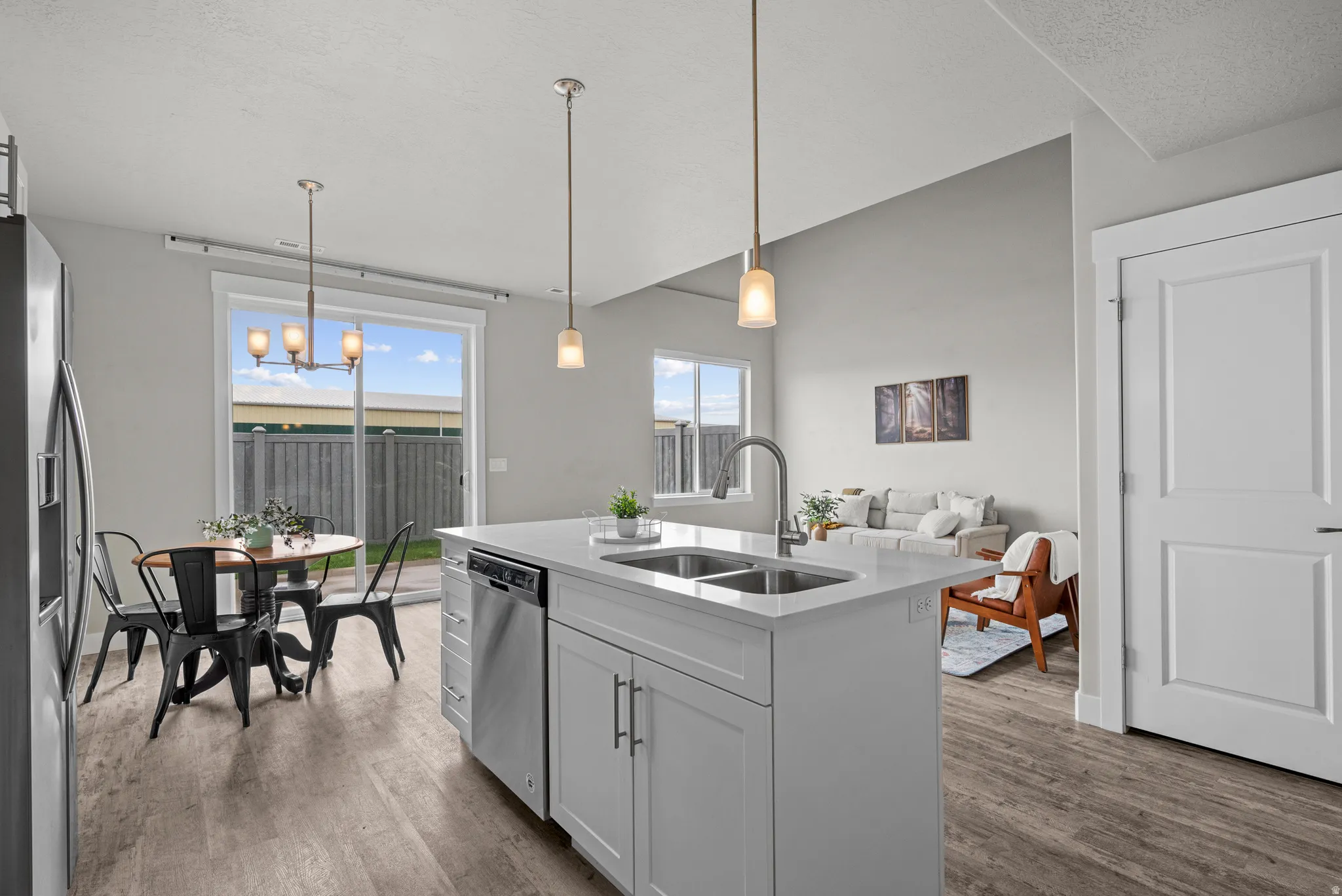 Kitchen featuring a kitchen island with sink, hanging light fixtures, dark wood finished floors, light stone counters, and a textured ceiling