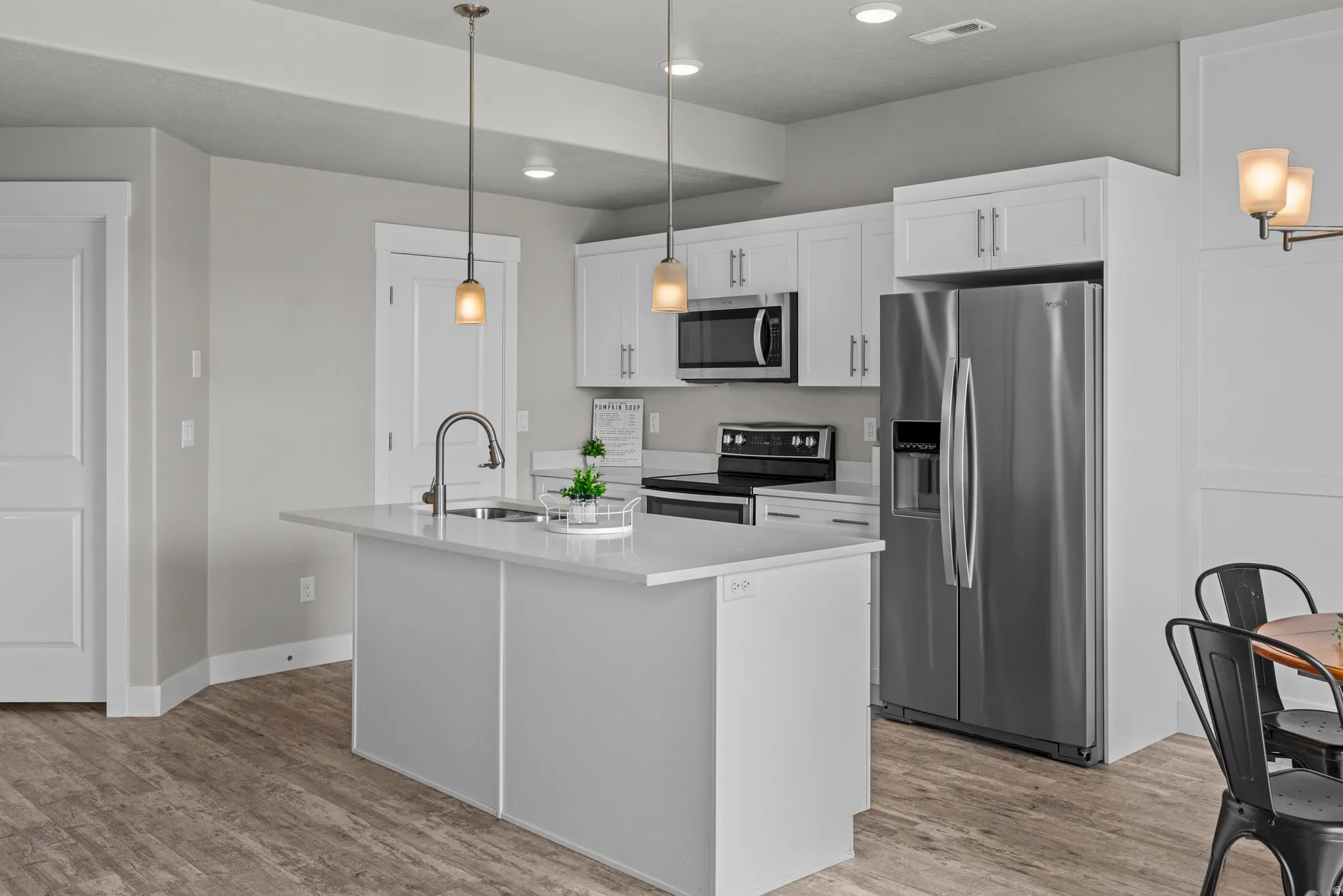 Kitchen with stainless steel appliances, white cabinets, an island with sink, light wood-style flooring, and decorative light fixtures