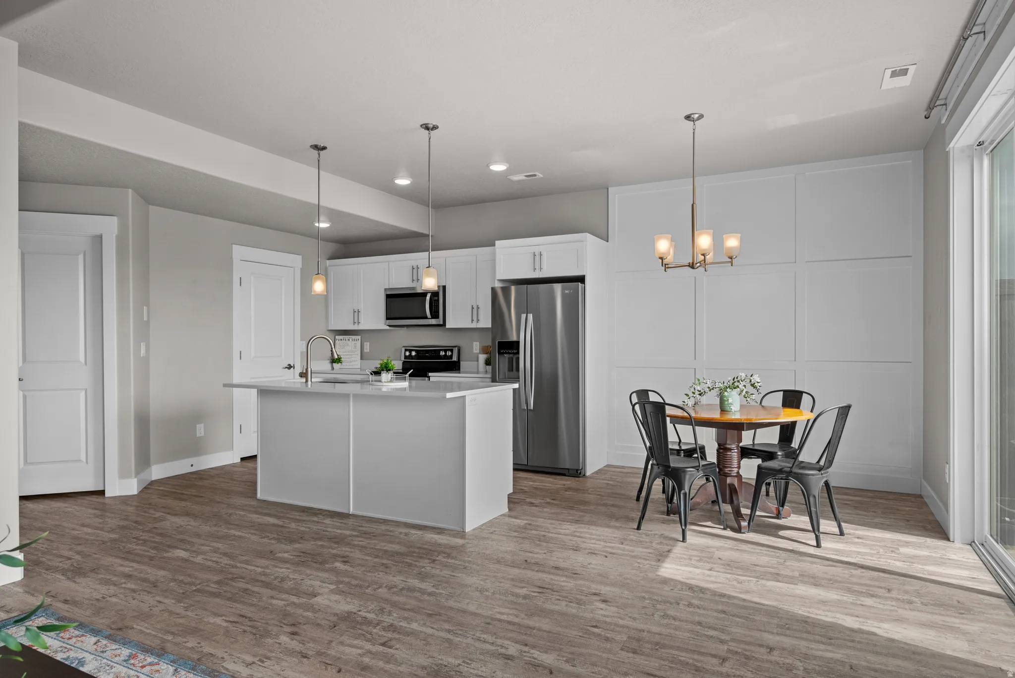 Kitchen featuring stainless steel appliances, white cabinetry, a kitchen island with sink, and dark wood-style floors