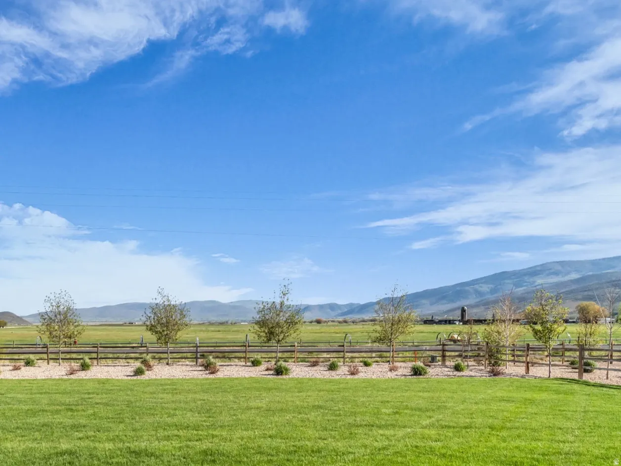 Expansive lawn area with a decorative split-rail fence, bordered by young trees and shrubbery