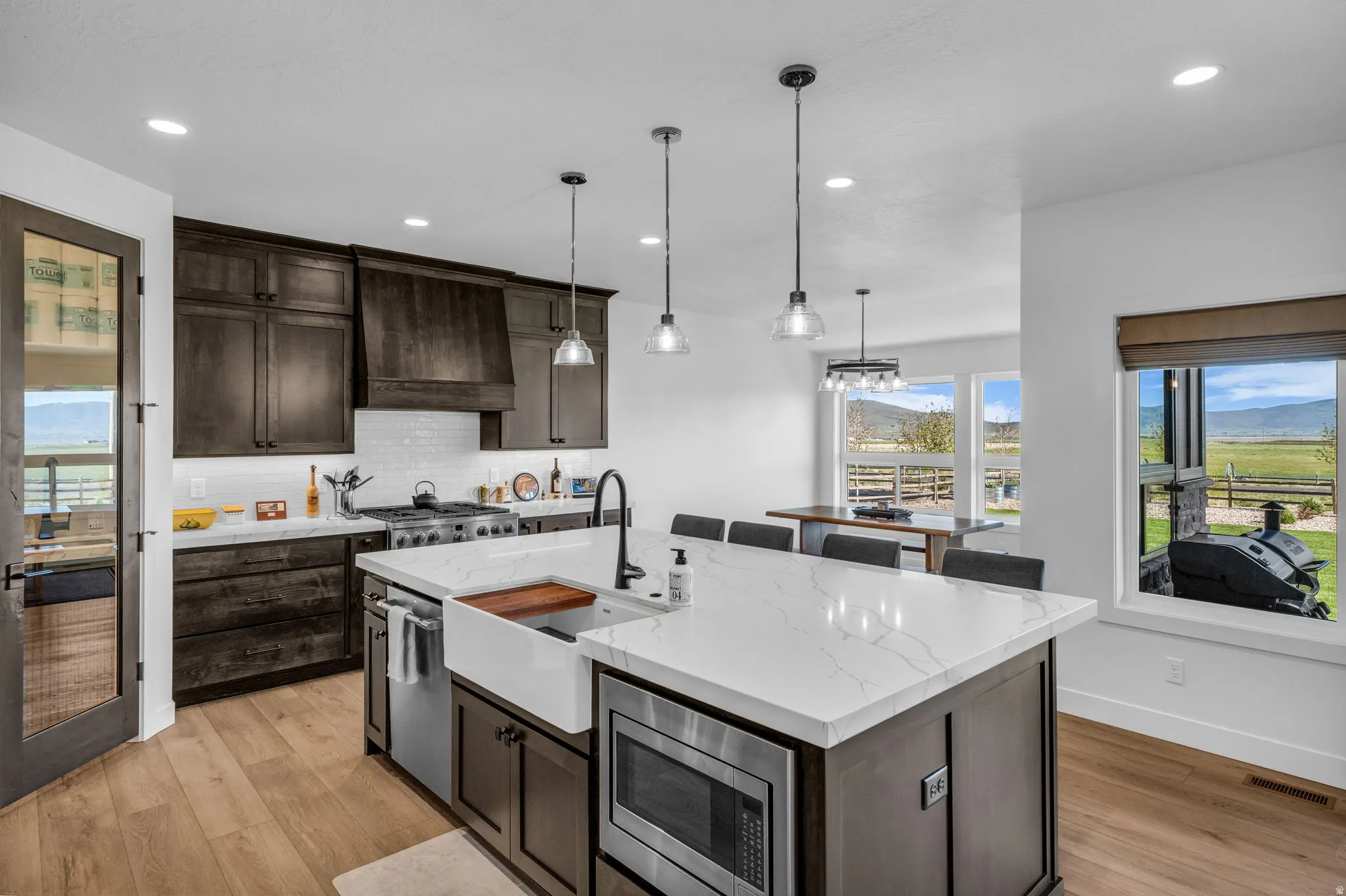 Spacious kitchen featuring an oversized island with a farmhouse sink, white quartz countertops, dark wood cabinetry, and stainless steel appliances
