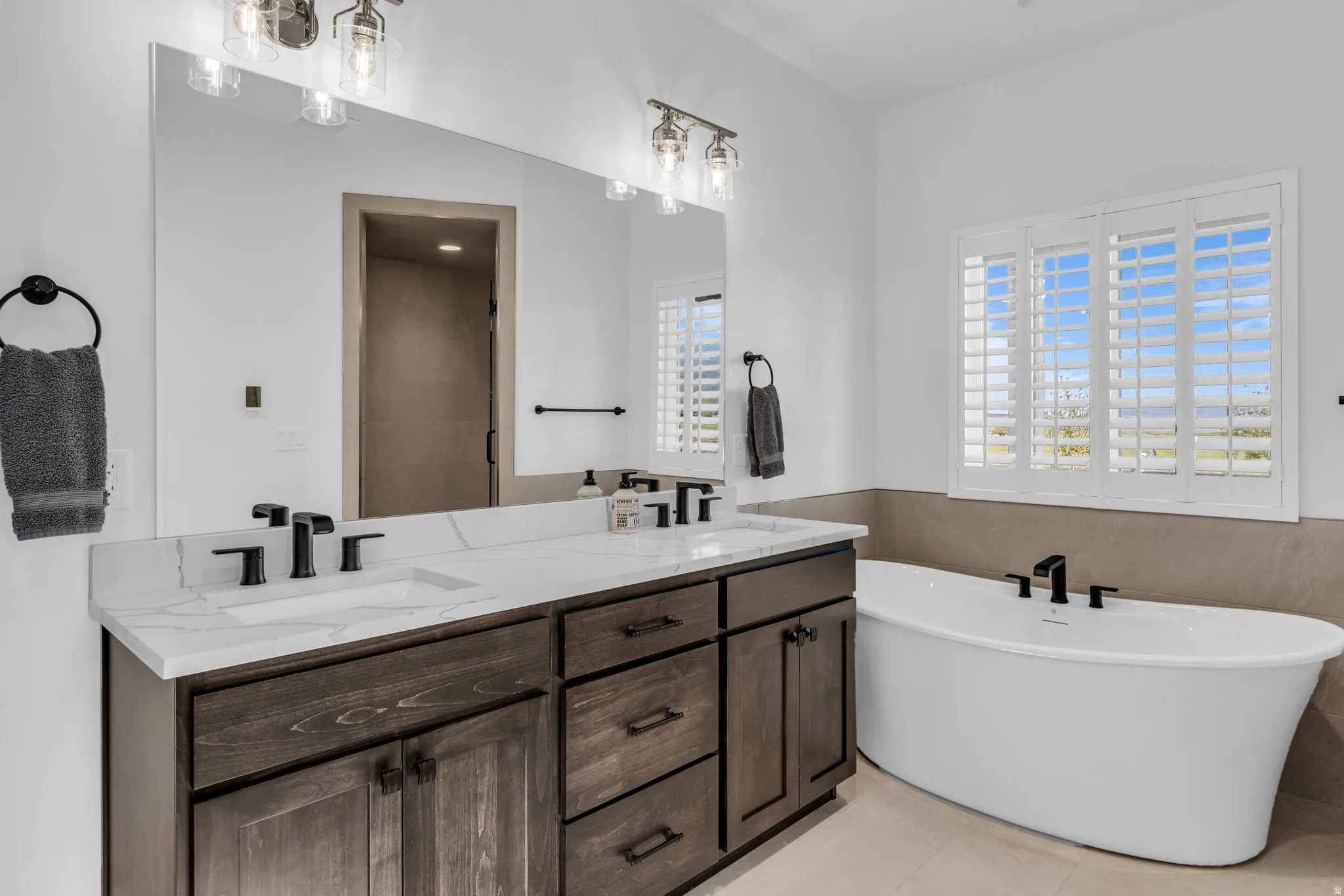 Bathroom featuring a dual-sink vanity with a white countertop, dark wood-finish cabinetry, and matte black fixtures