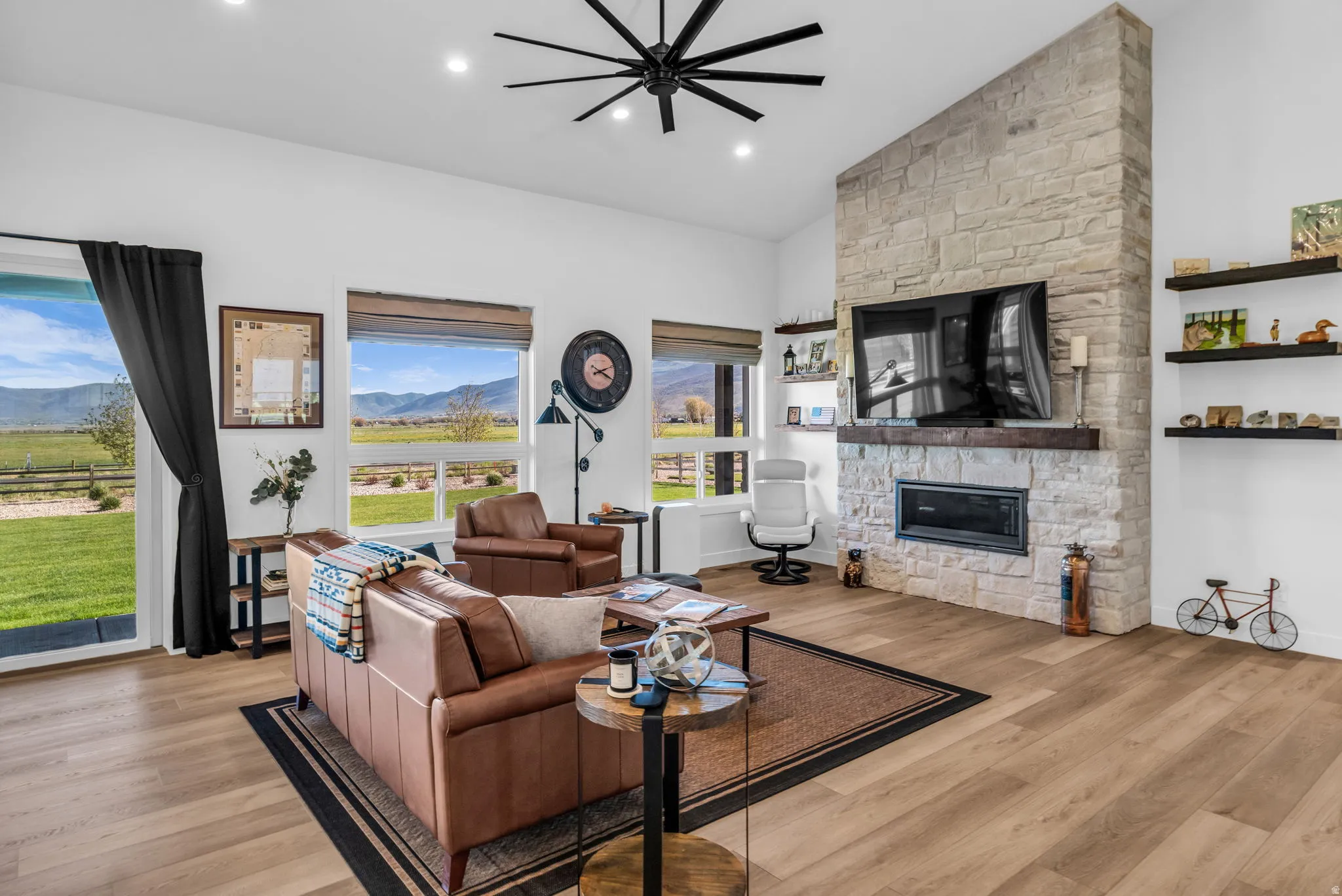 Spacious living area featuring a stone-clad fireplace with a wood mantel, wood-finish flooring, recessed lighting, and a modern ceiling fan