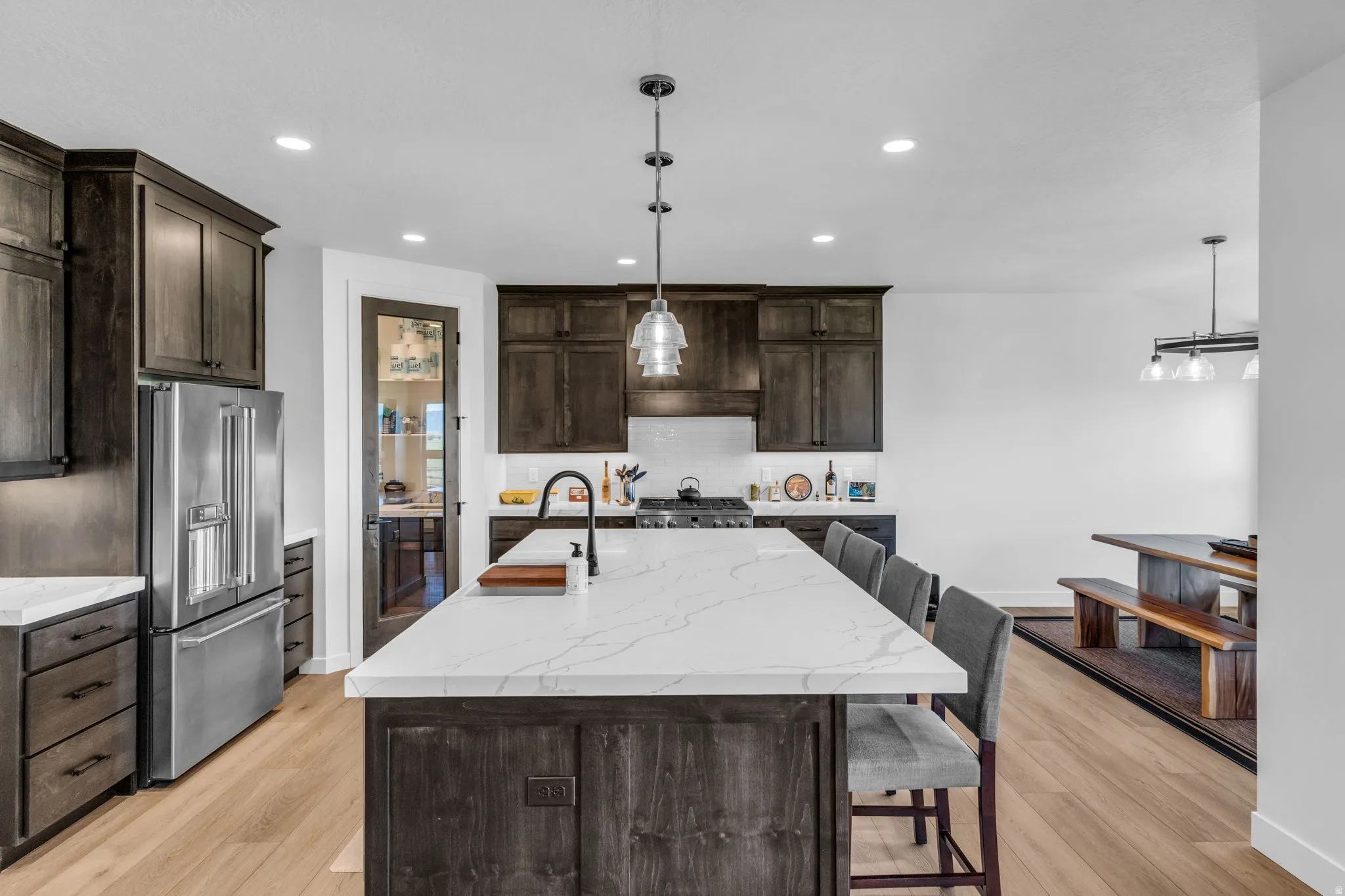 Spacious kitchen featuring an oversized island with countertop seating, stainless steel appliances, dark wood-finish cabinetry, and recessed lighting