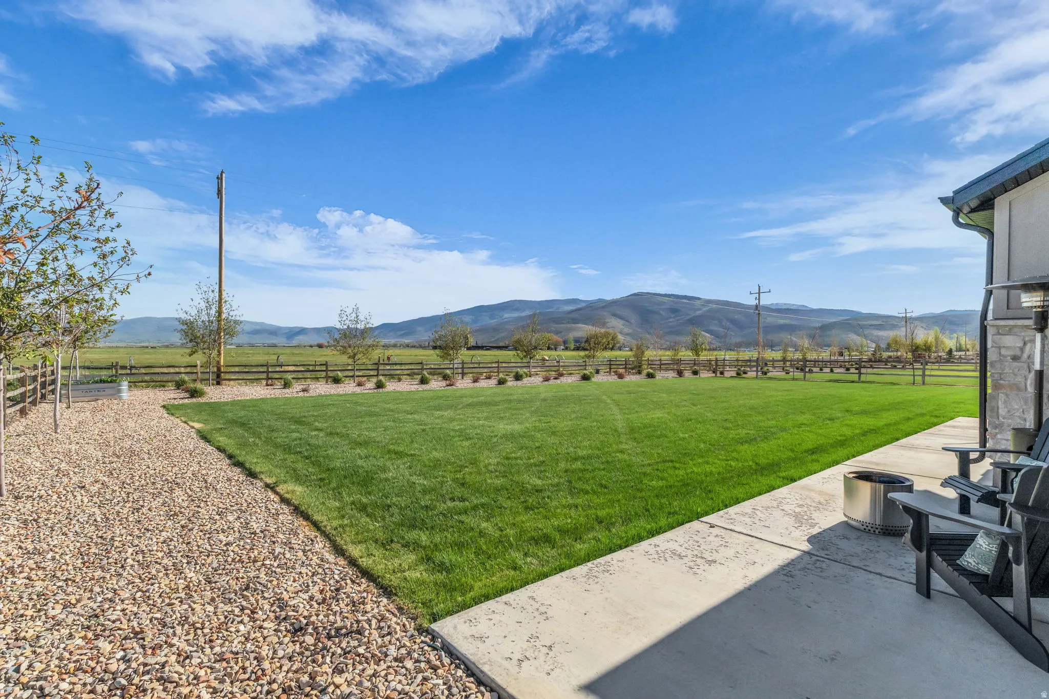 Expansive lawn with a concrete patio, gravel pathway, and a perimeter fence