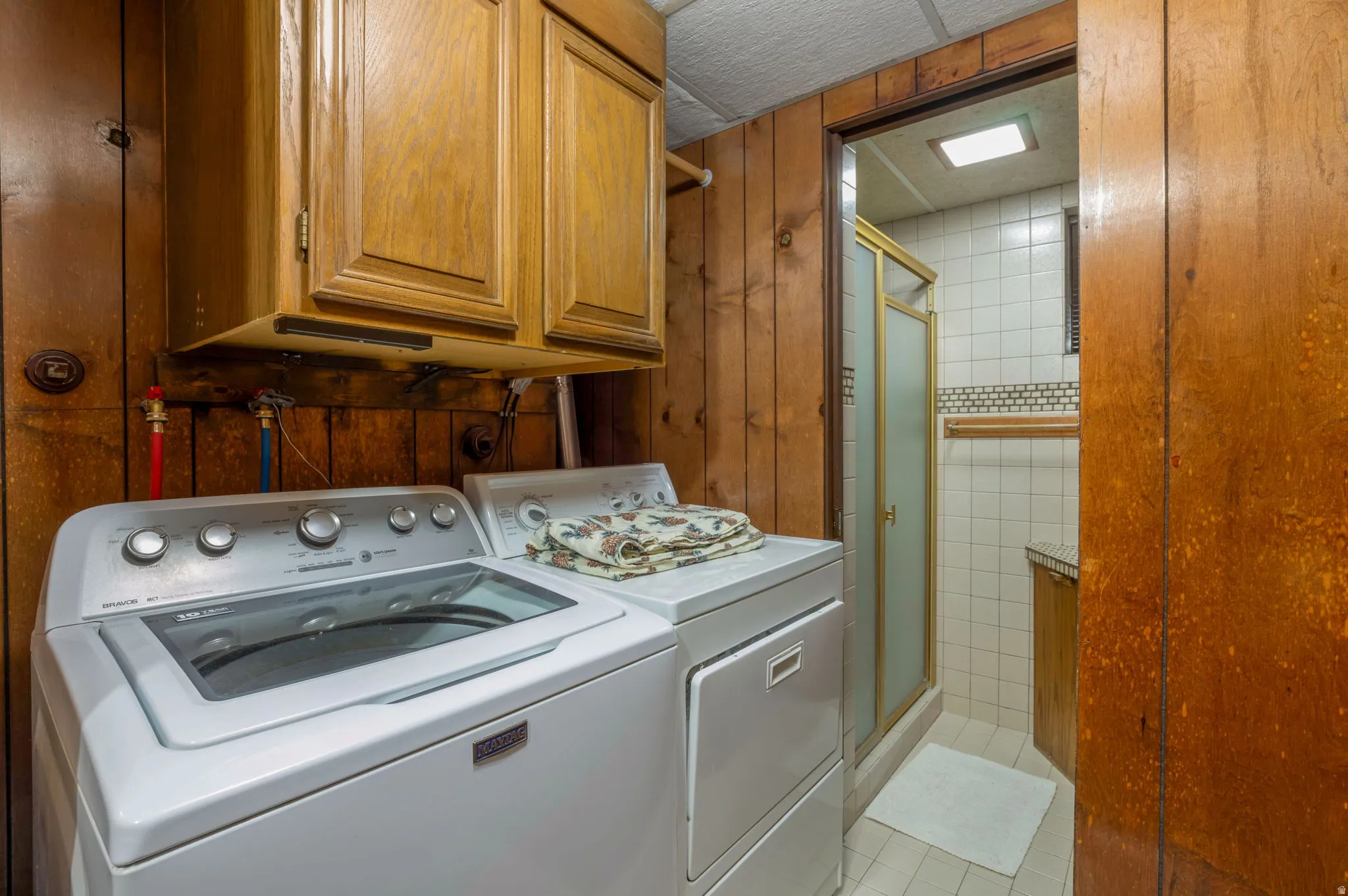 Laundry room featuring cabinet space, light tile patterned floors, wood walls, and separate washer and dryer