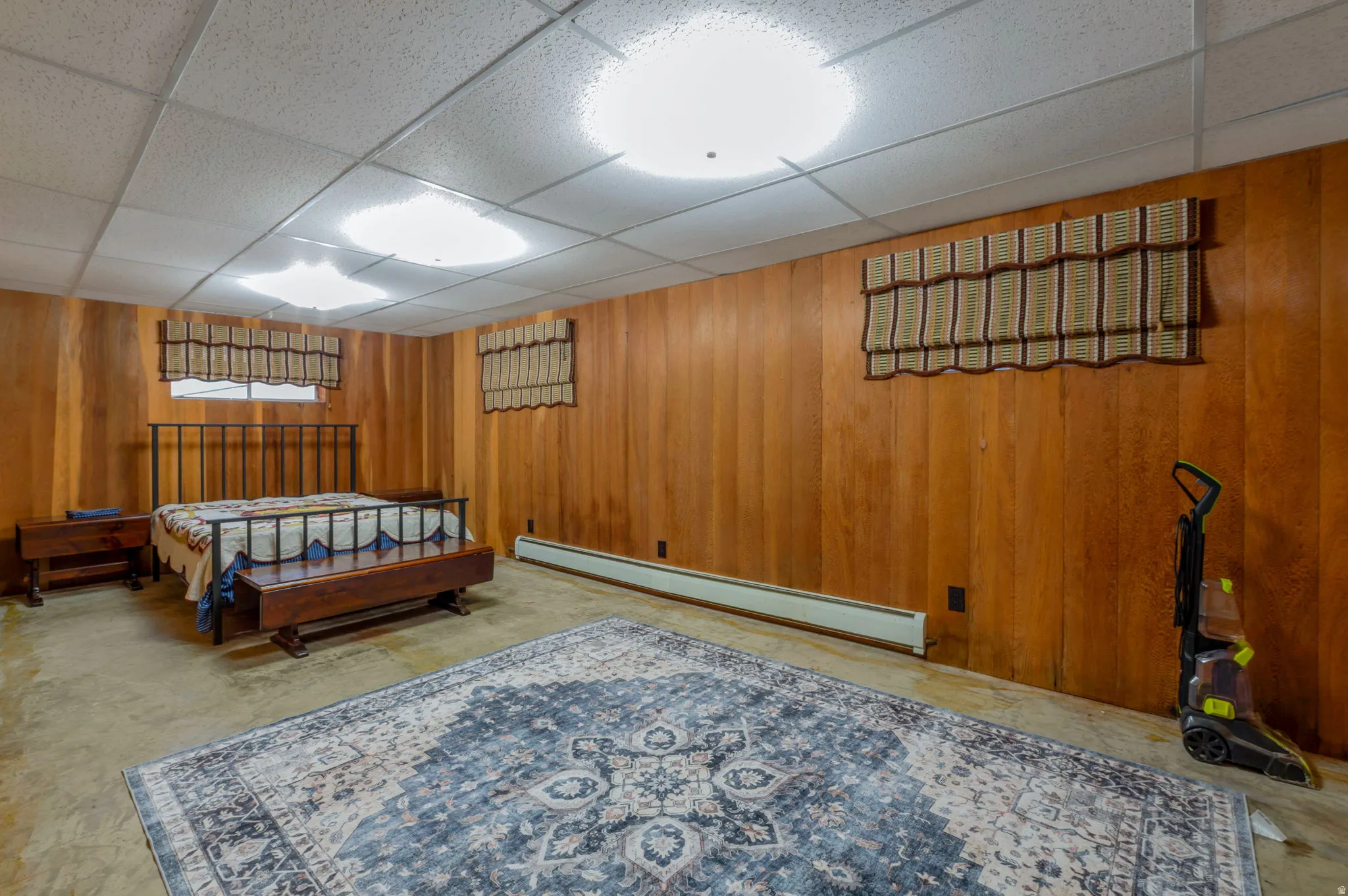 Bedroom with wooden walls, a drop ceiling, and a baseboard heating unit