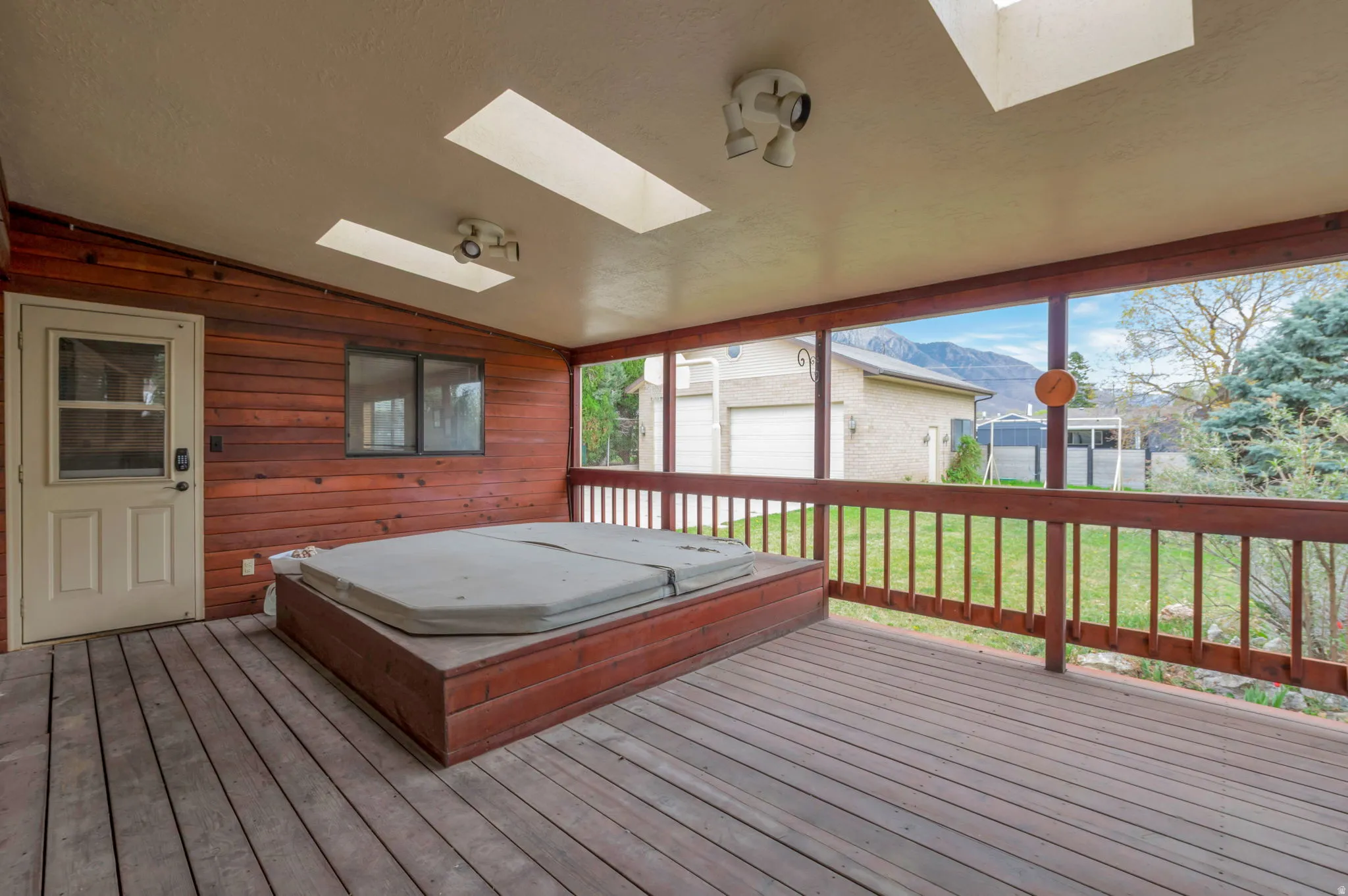 Deck with a covered hot tub, a lawn, a mountain view, and an outbuilding
