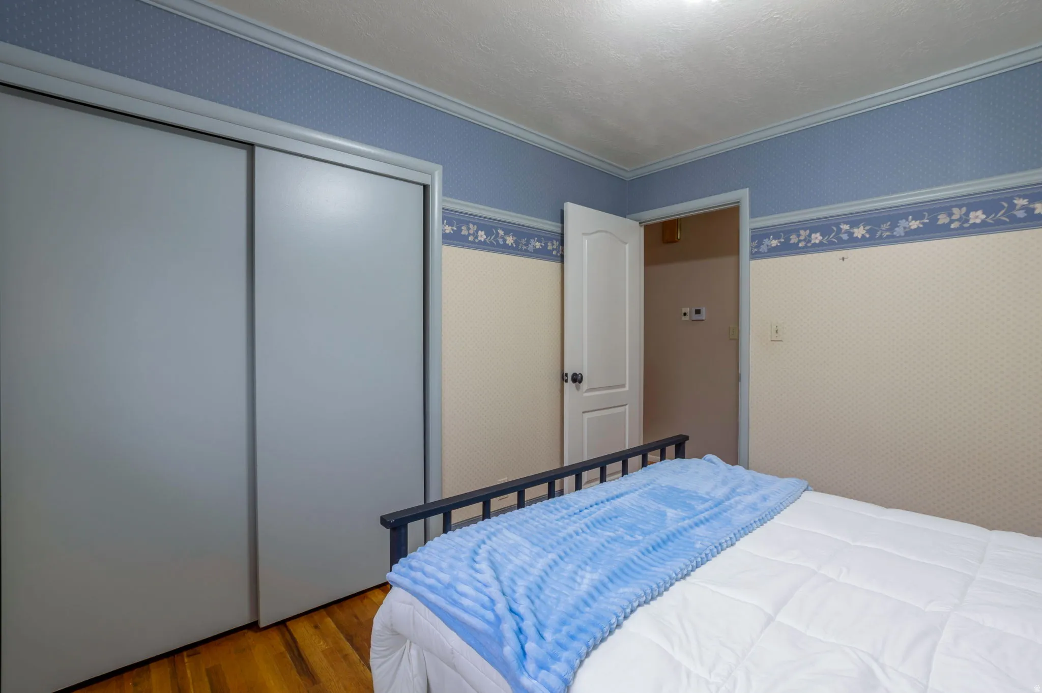Bedroom featuring wallpapered walls, a closet, wood finished floors, and crown molding