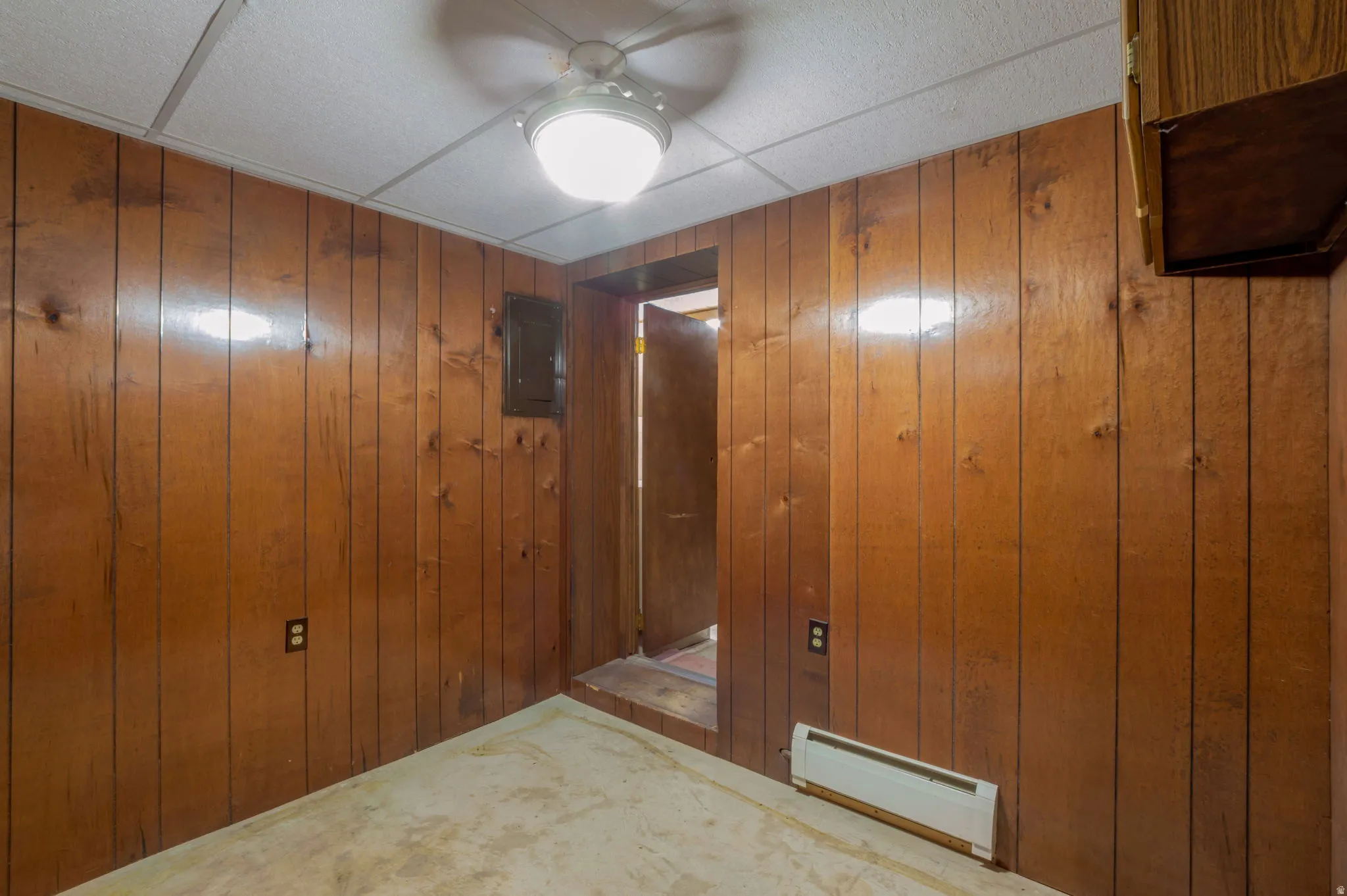 Hall featuring a baseboard radiator, wood walls, electric panel, and carpet flooring