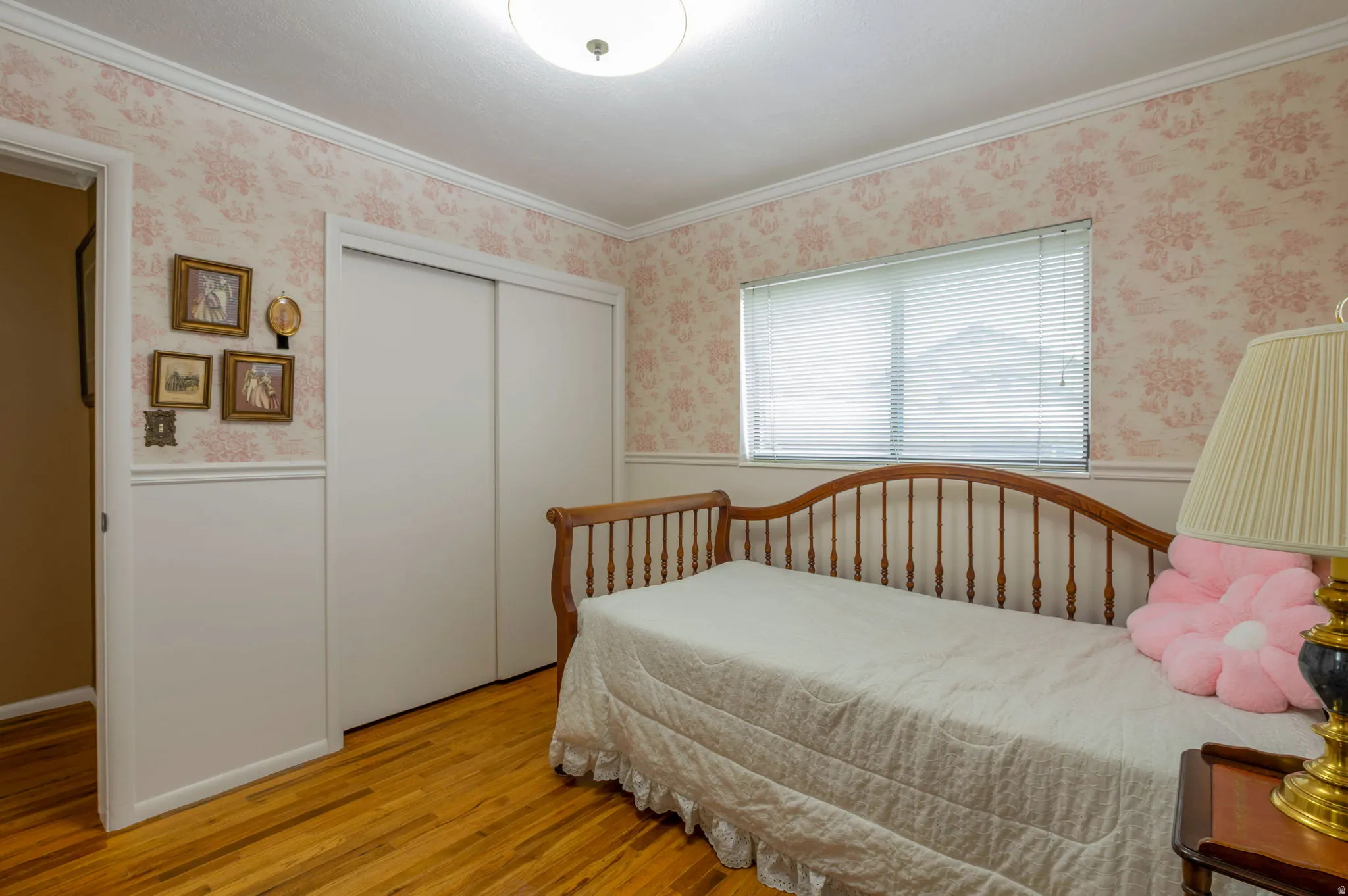 Bedroom featuring wood finished floors, crown molding, a wainscoted wall, a closet, and wallpapered walls