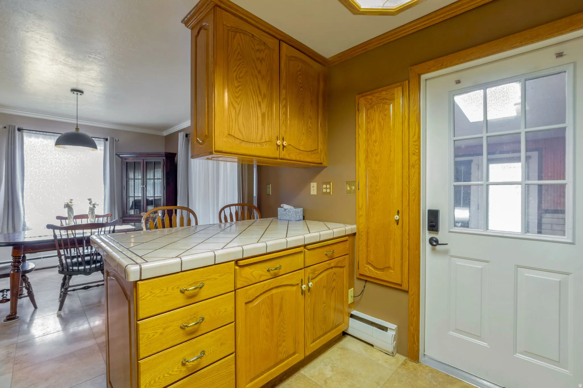 Kitchen featuring ornamental molding, a baseboard heating unit, tile counters, plenty of natural light, and wood finish cabinets