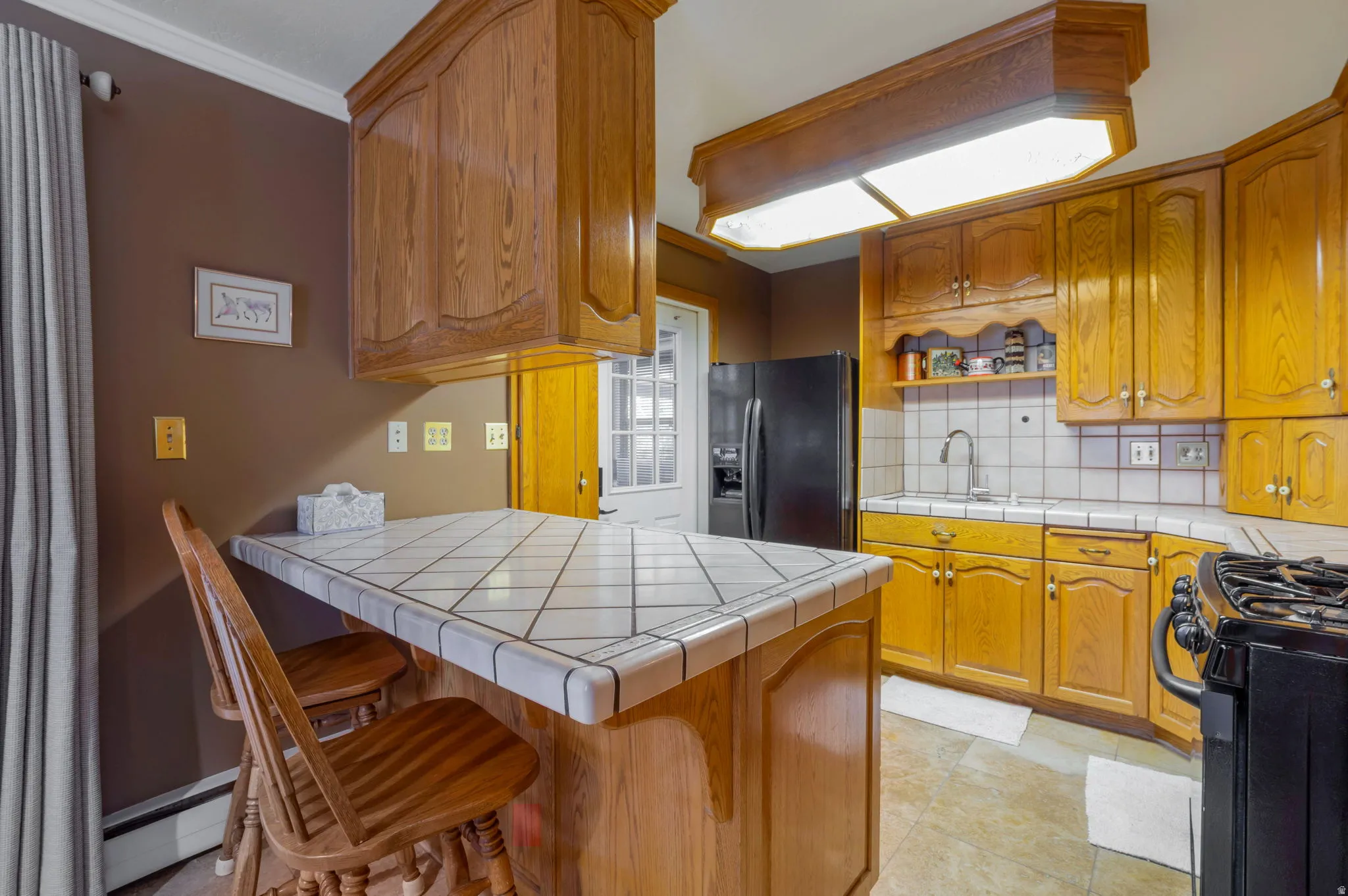 Kitchen featuring tile counters, a peninsula, a kitchen bar, backsplash, and ornamental molding