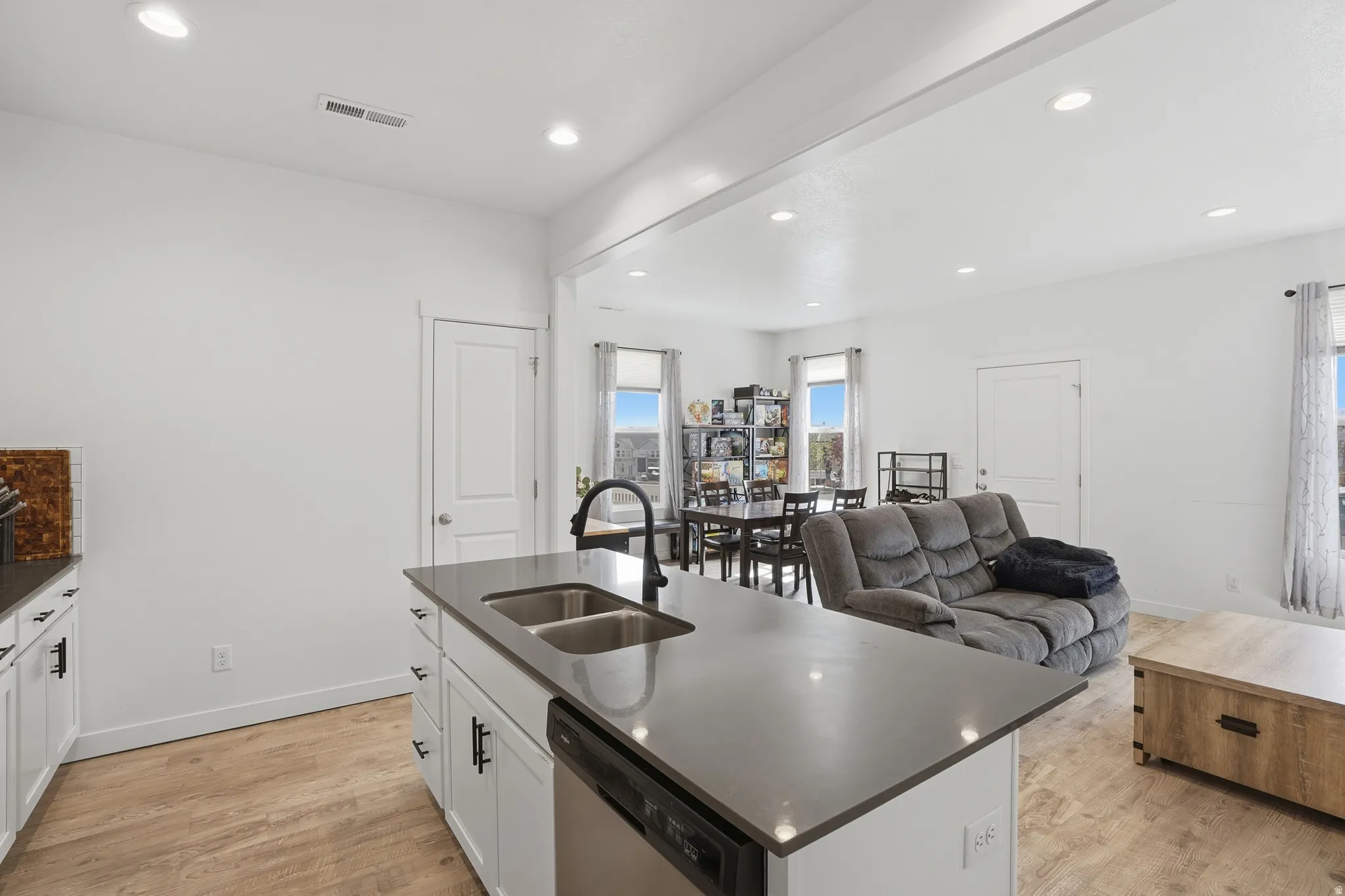 Kitchen featuring dark countertops, open floor plan, an island with sink, white cabinets, and stainless steel dishwasher