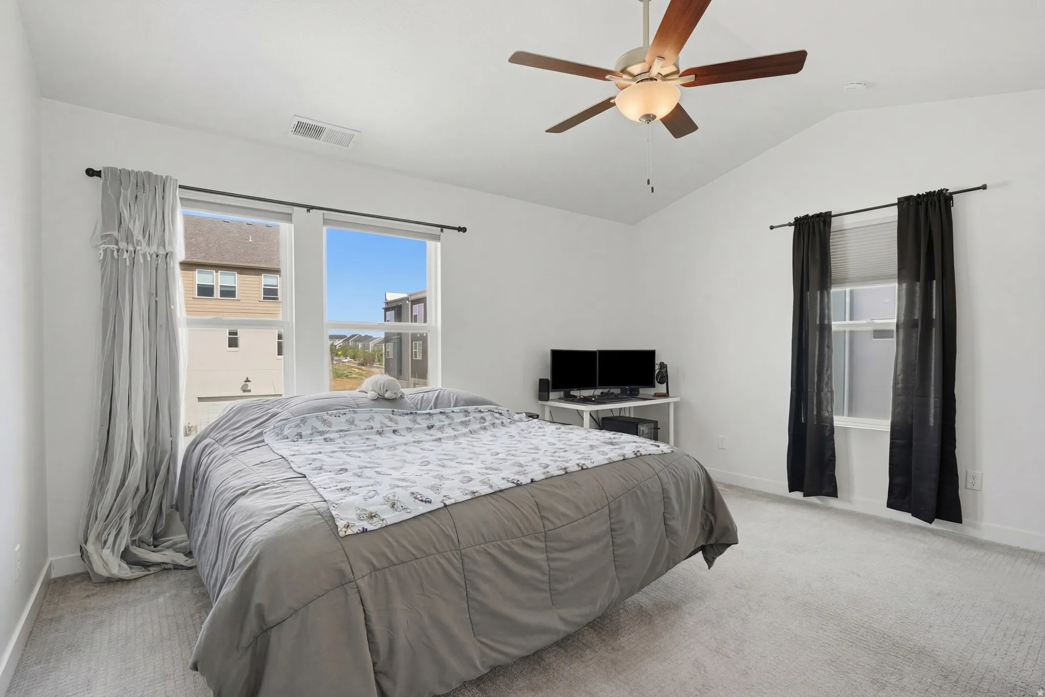 Primary bedroom featuring vaulted ceiling, light colored carpet, and a ceiling fan