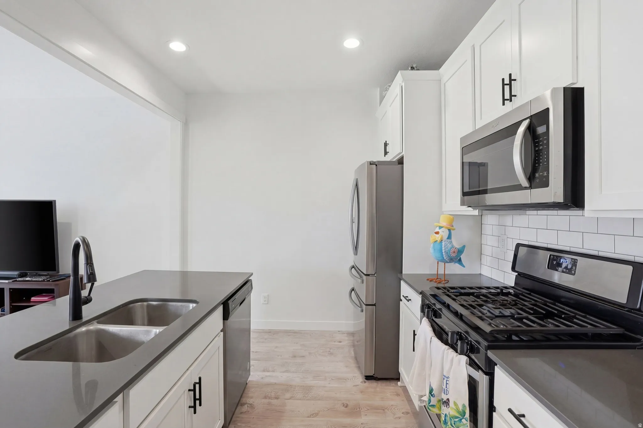 Kitchen featuring stainless steel appliances, white cabinetry, light wood-style floors, dark stone countertops, and recessed lighting