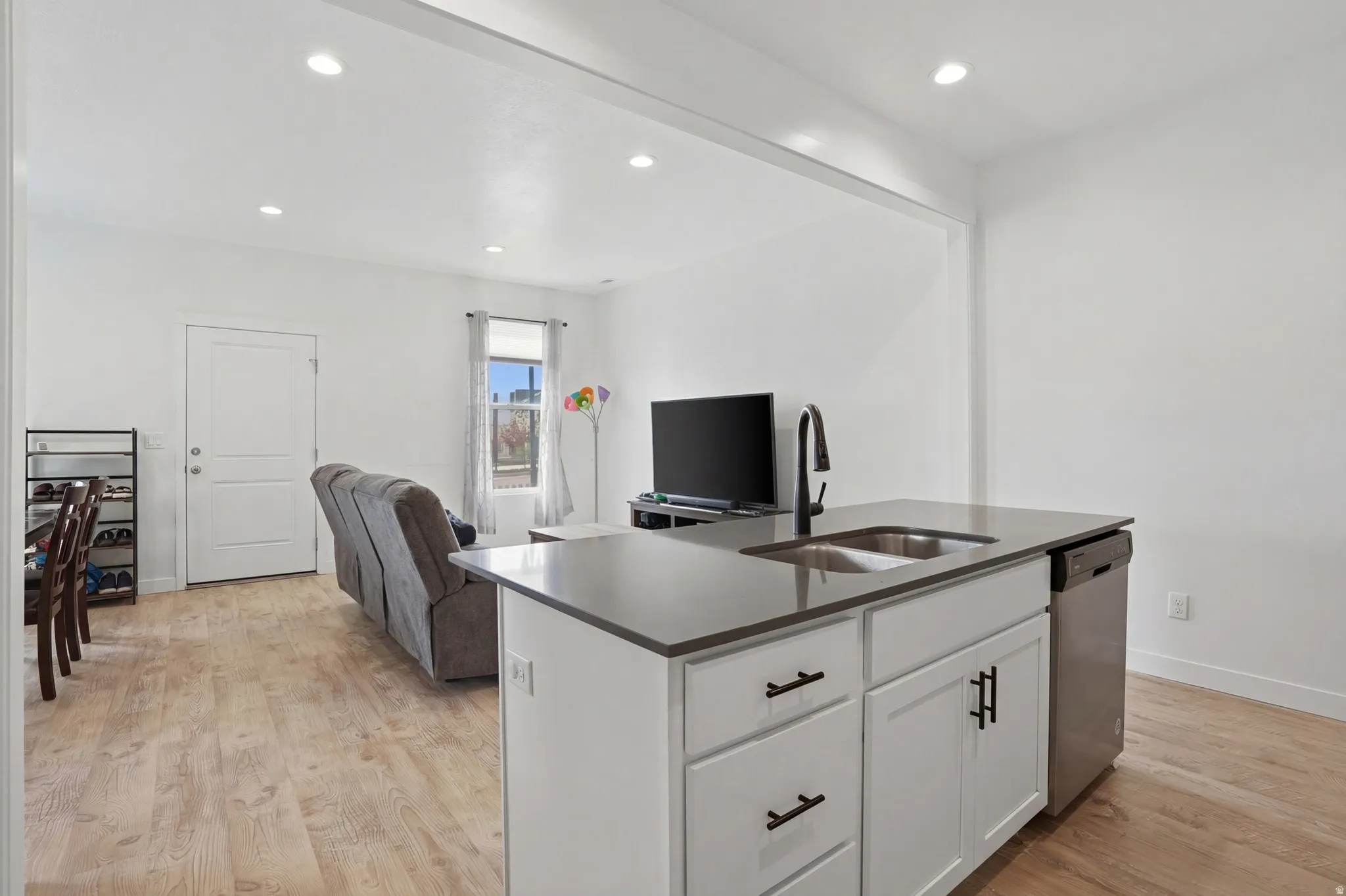 Kitchen featuring open floor plan, white cabinetry, a kitchen island with sink, light wood finished floors, and dishwasher
