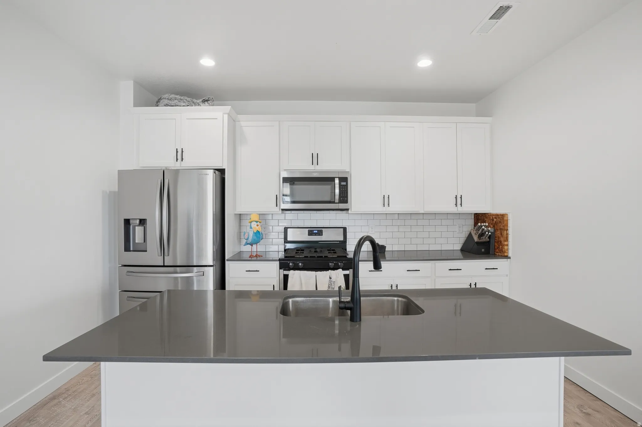 Kitchen featuring stainless steel appliances, white cabinetry, light wood-style floors, backsplash, and an island with sink
