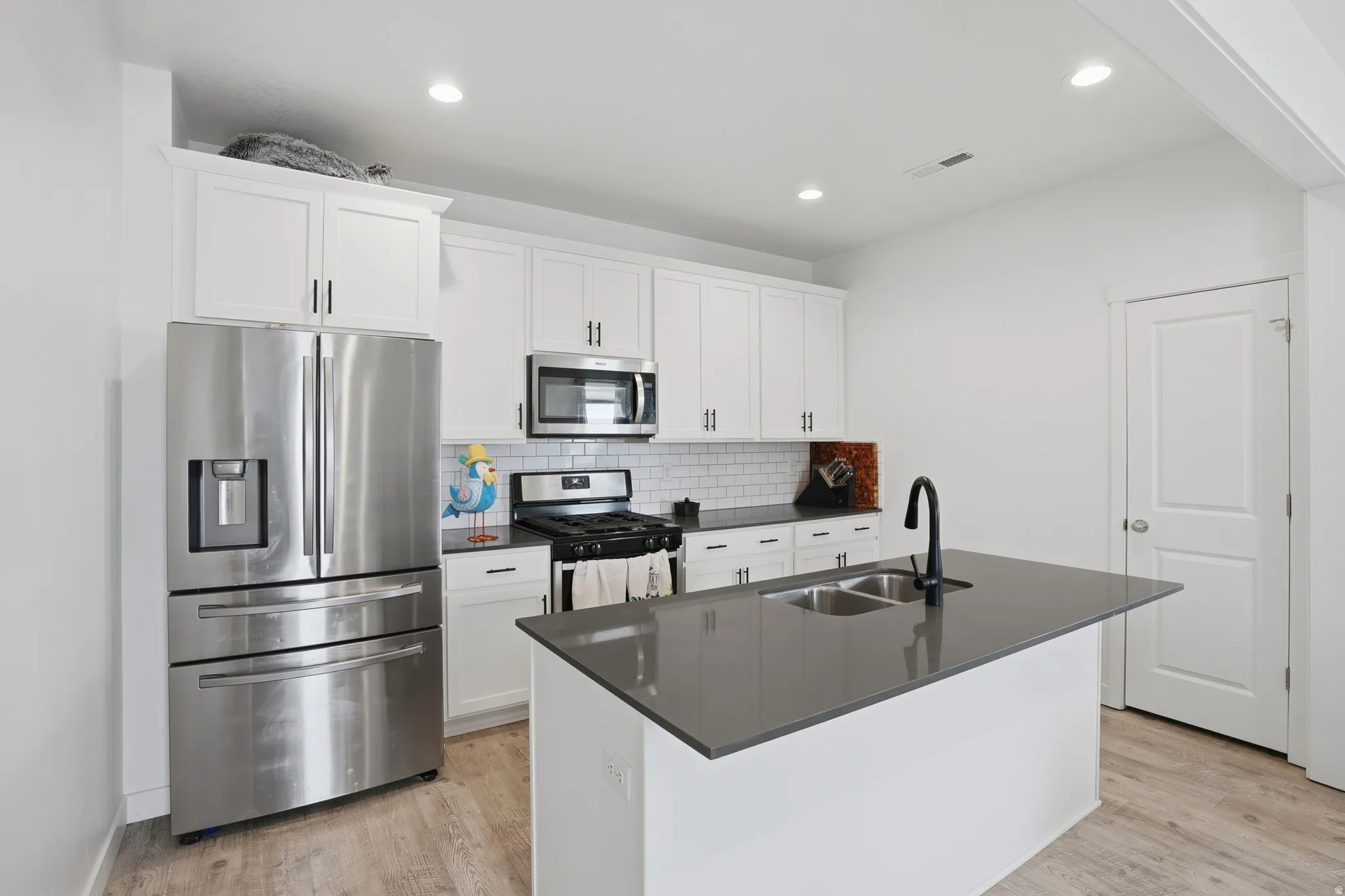 Kitchen featuring stainless steel appliances, white cabinets, a center island with sink, light wood finished floors, and recessed lighting
