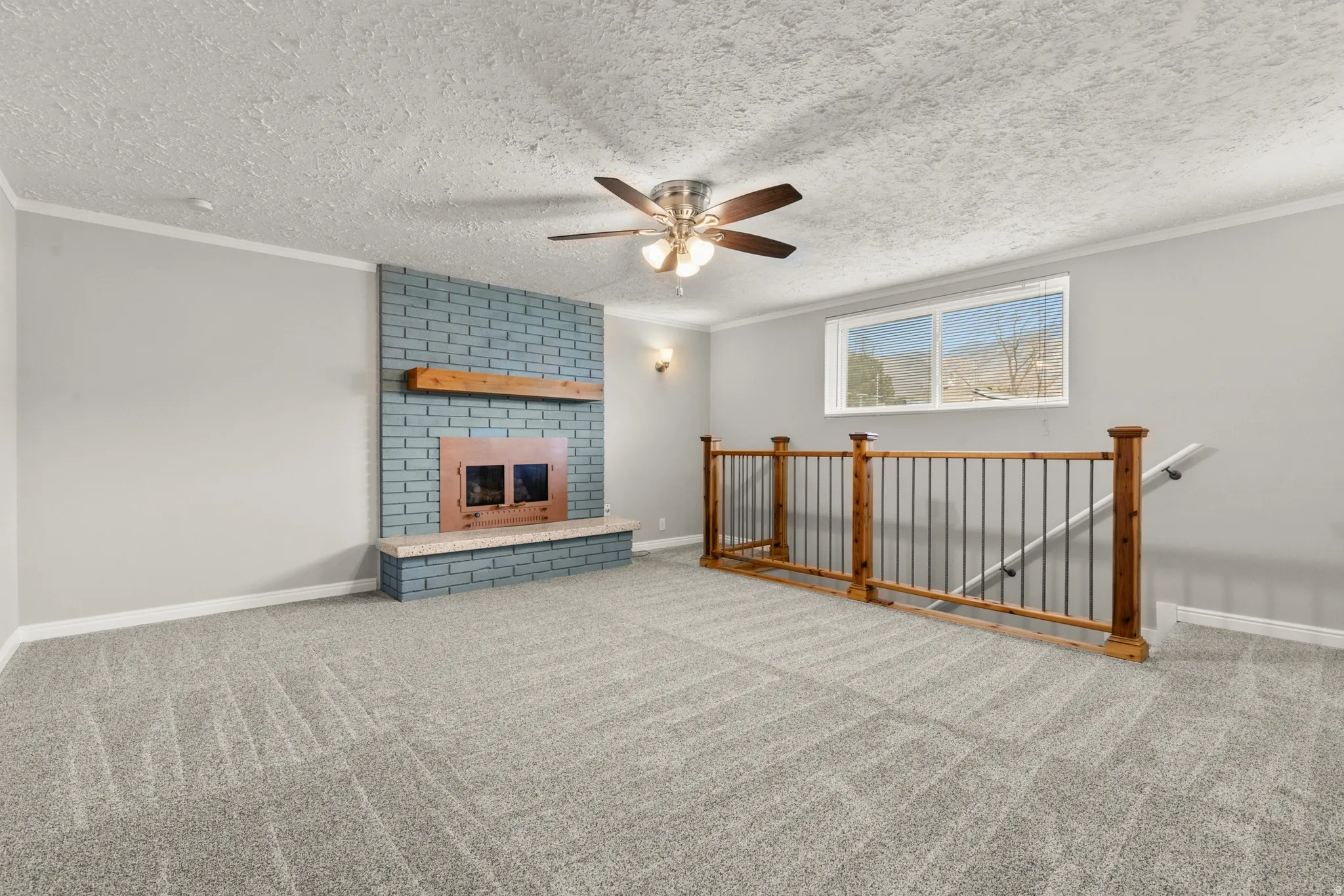Unfurnished living room featuring carpet flooring, a fireplace, ceiling fan, a textured ceiling, and ornamental molding