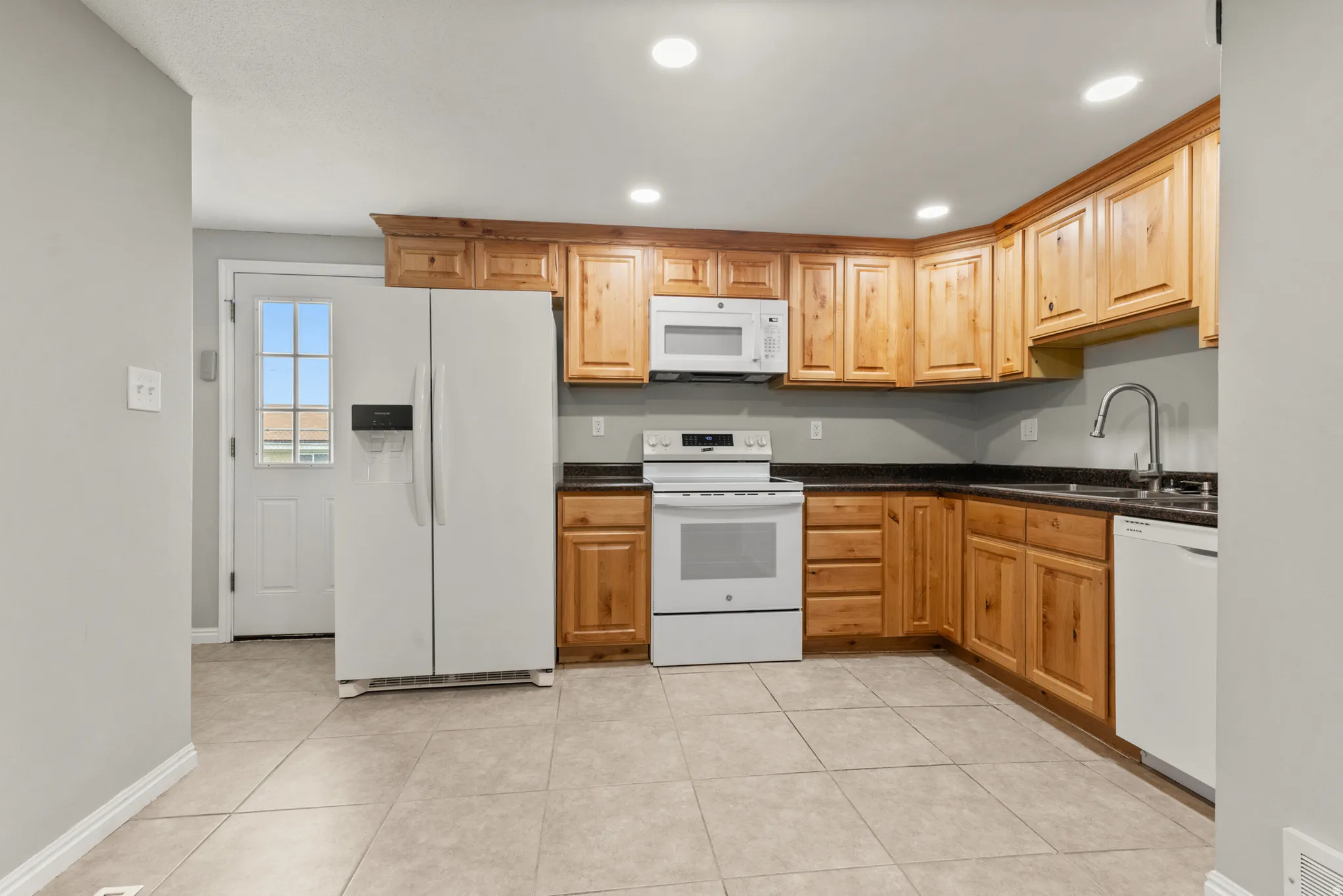 Kitchen with white appliances, recessed lighting, light tile patterned flooring, and dark stone countertops