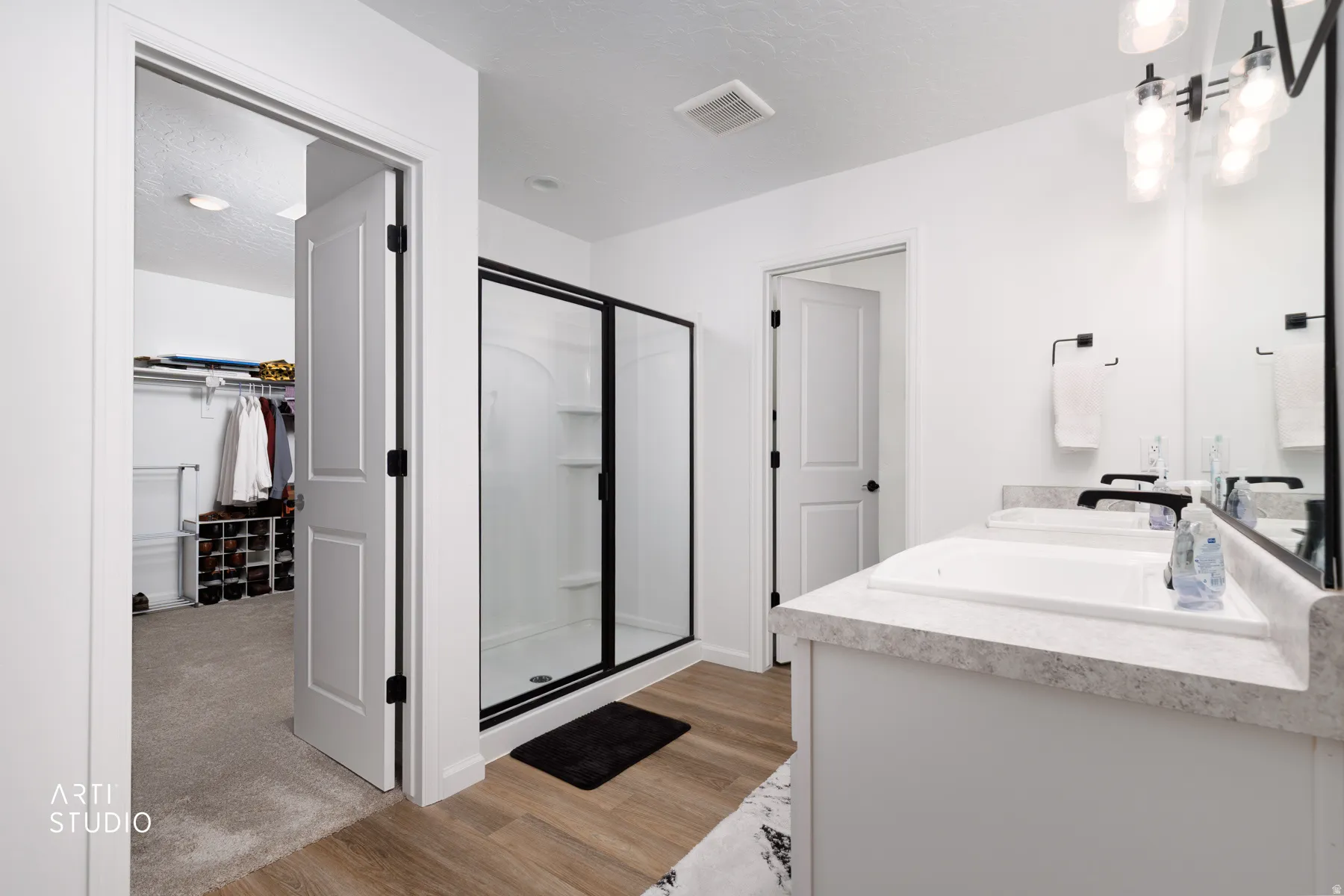 Bathroom featuring double vanity, a stall shower, a spacious closet, and light wood finished floors