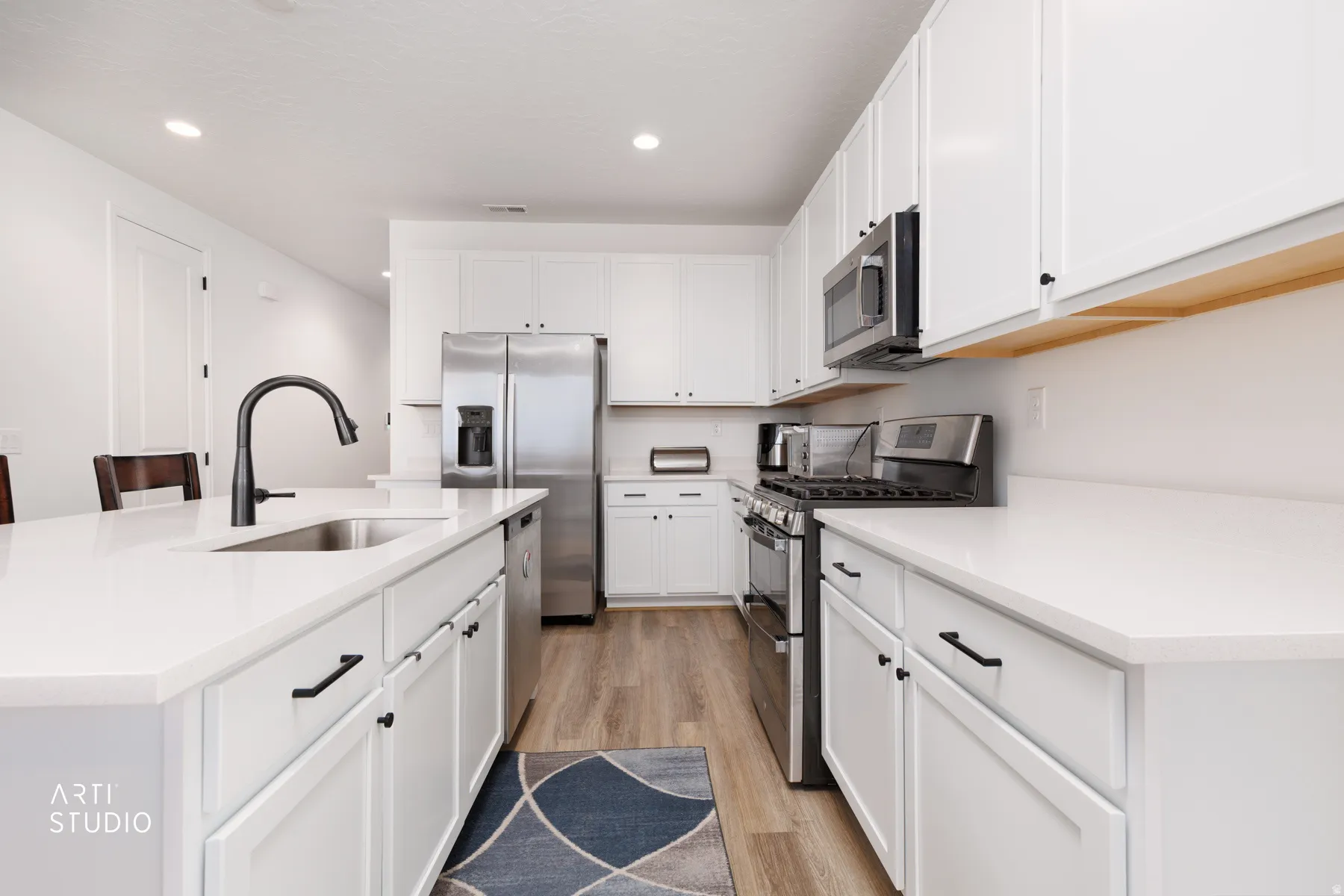Kitchen with stainless steel appliances, a center island with sink, light wood-style floors, recessed lighting, and white cabinets
