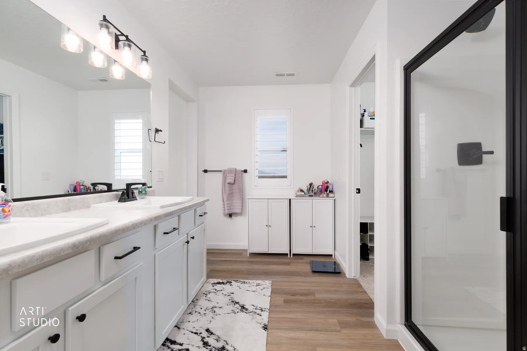 Bathroom with double vanity, a stall shower, and light wood-type flooring