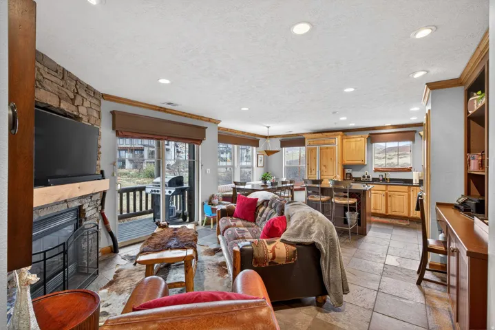 Living room featuring a stone fireplace, stone tile flooring, crown molding, a textured ceiling, and recessed lighting