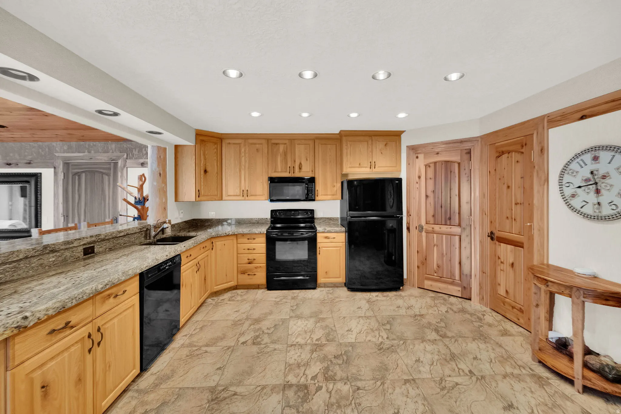 Kitchen featuring light stone countertops, black appliances, light wood finish cabinetry, and recessed lighting