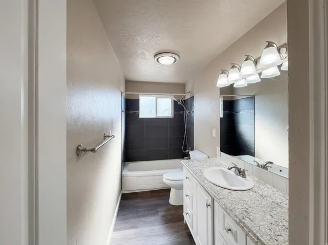 Bathroom featuring vanity, a textured ceiling, shower / tub combination, dark wood-style flooring, and a textured wall