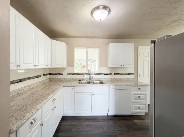 Kitchen featuring freestanding refrigerator, white cabinetry, light countertops, a textured ceiling, and dark wood finished floors