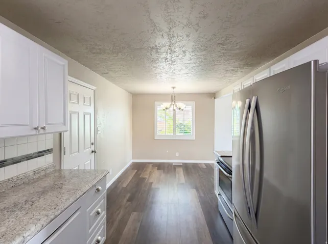 Kitchen featuring stainless steel appliances, light countertops, white cabinets, suspended lighting, and dark wood-type flooring