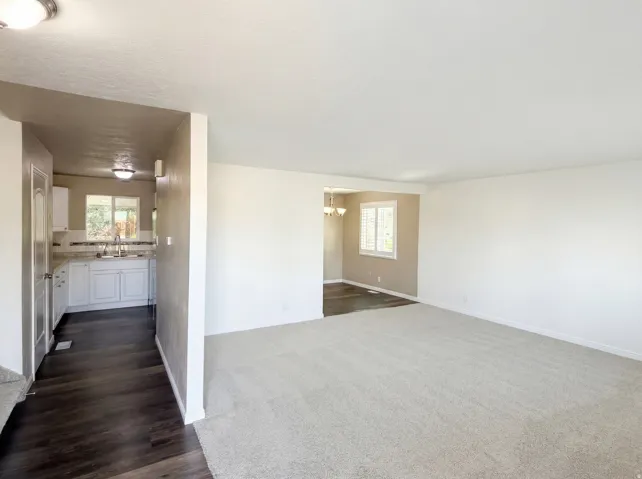 Empty room with hanging lights, dark colored carpet, and dark wood-style flooring