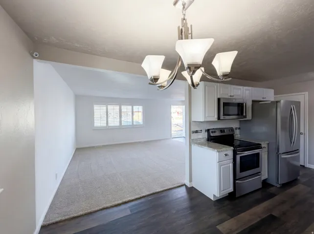 Kitchen with stainless steel appliances, white cabinetry, open floor plan, and dark wood-type flooring