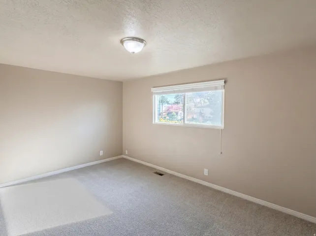 Carpeted empty room with a textured ceiling and baseboards