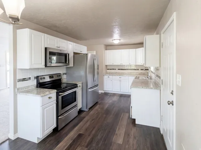 Kitchen featuring stainless steel appliances, white cabinetry, tasteful backsplash, dark wood finished floors, and a textured ceiling