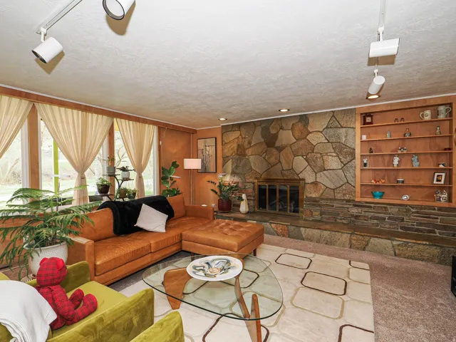 Living room with a textured ceiling, built in shelves, a stone fireplace, and carpet