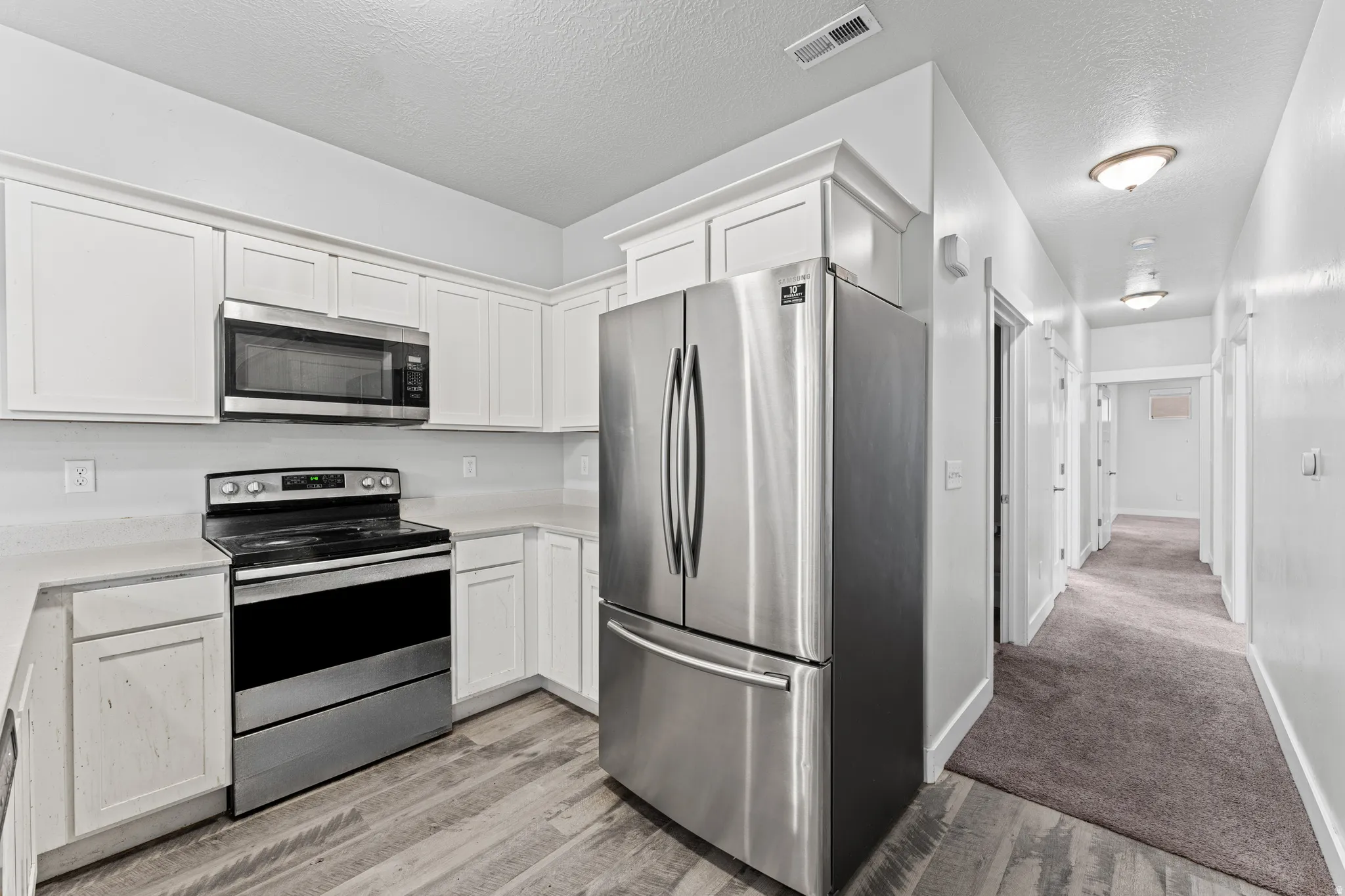 Kitchen with stainless steel appliances, light countertops, a textured ceiling, and white cabinetry